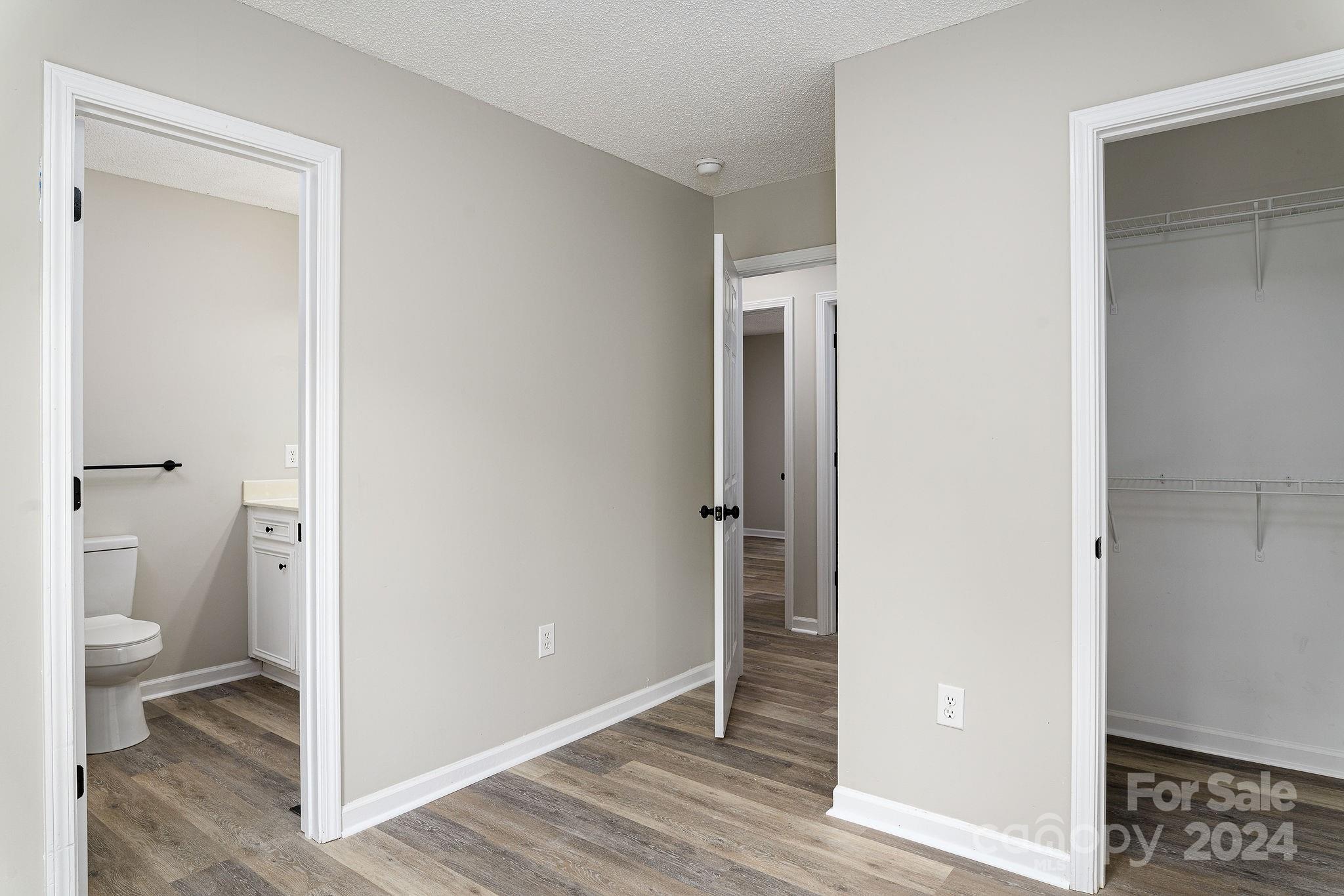 Empty bedroom with wood-look flooring, an open closet, and a bathroom doorway.