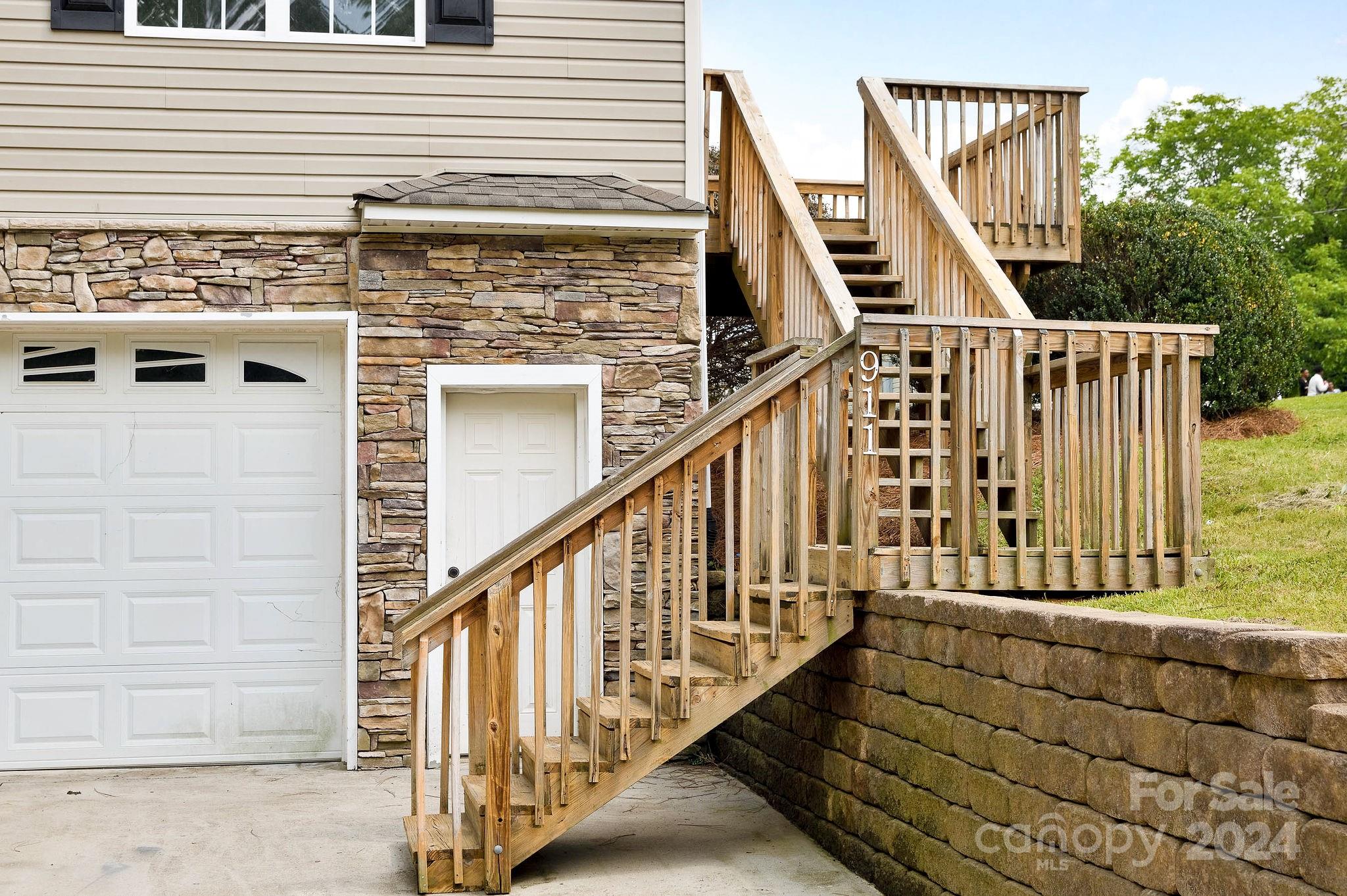 House exterior with a wooden staircase and landing beside stone facing and a garage door.