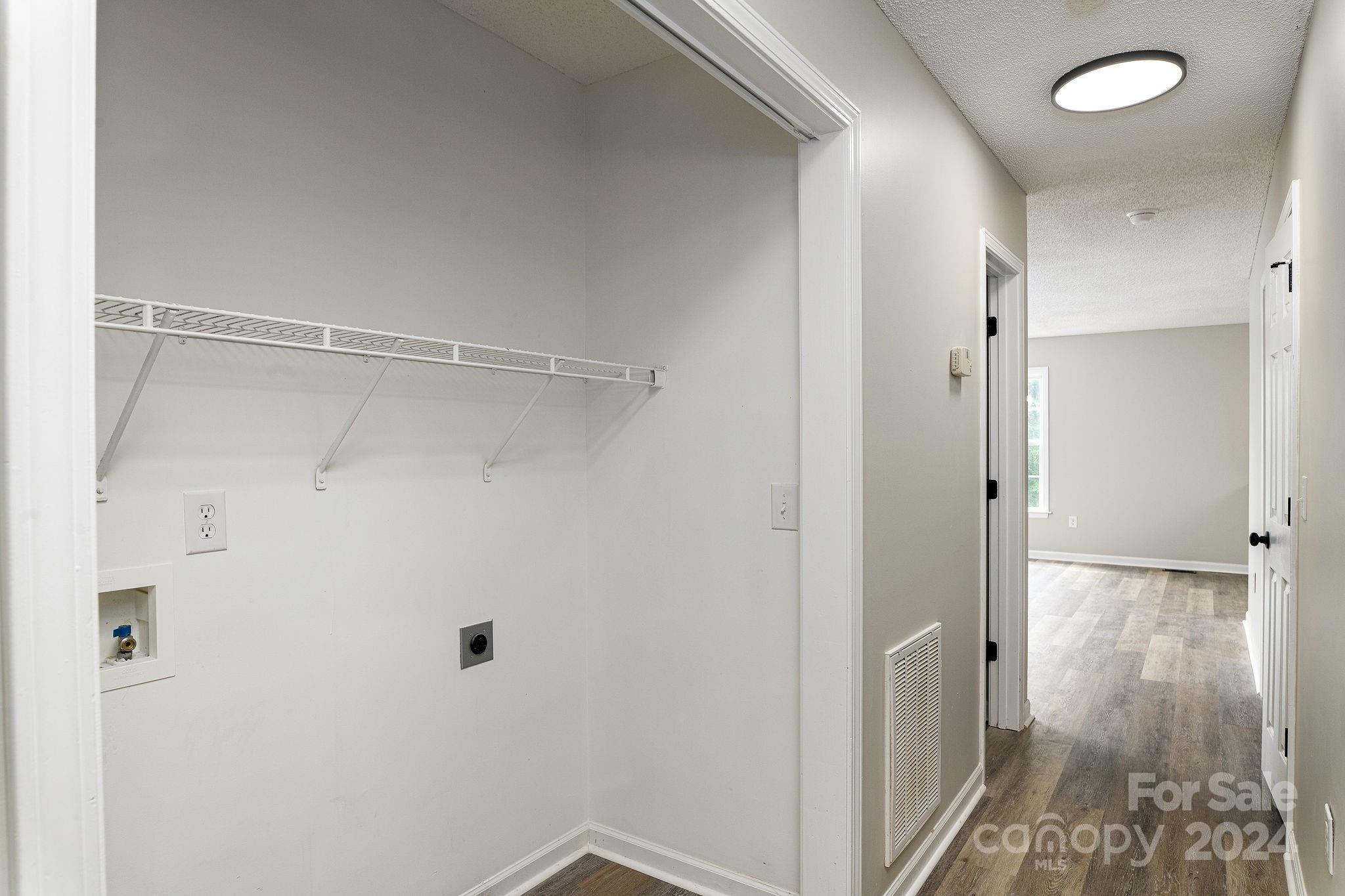 Empty laundry closet with wire shelf and washer hookups opening onto a hallway.