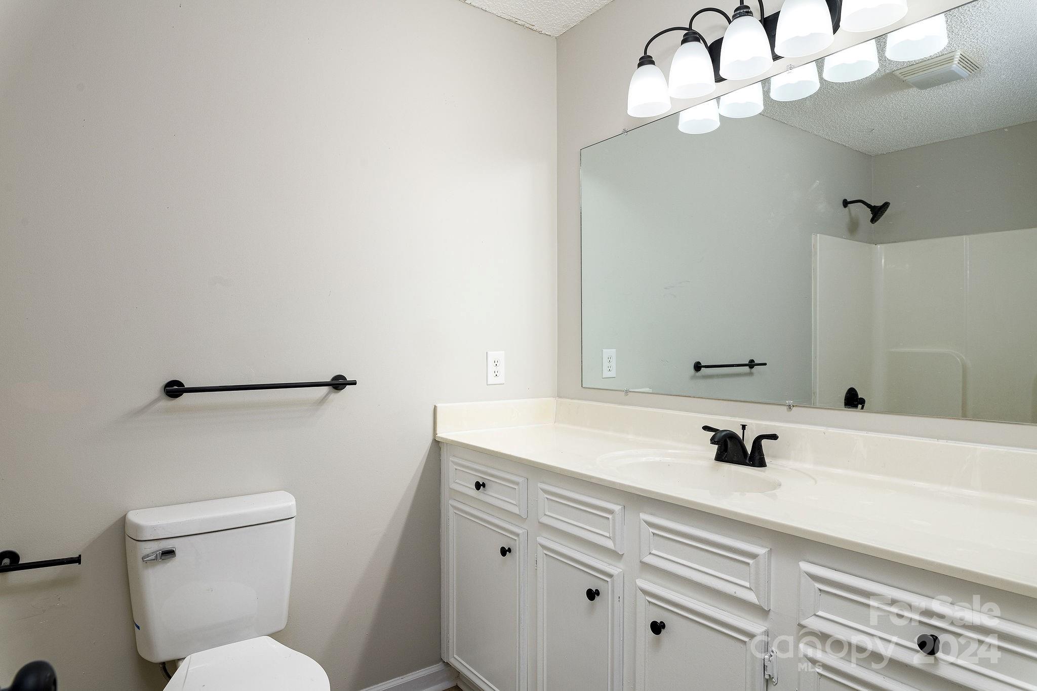 Bathroom with a long white vanity, large mirror, black fixtures, and toilet.