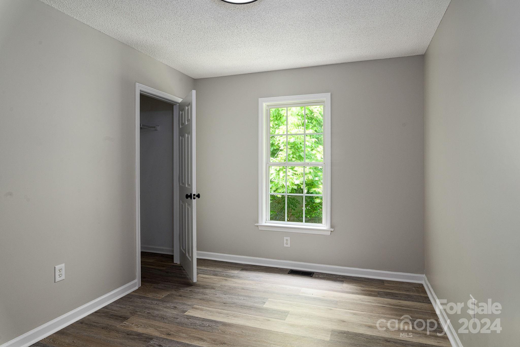 Empty room with dark wood-look flooring, a leafy window, and an open closet door.