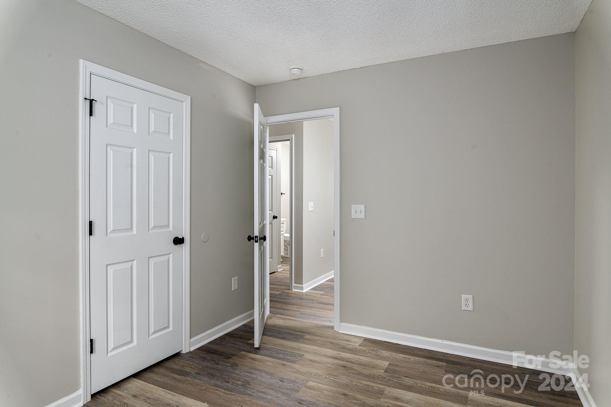 Empty room with gray walls, dark wood-look flooring, and open doors to a hallway.