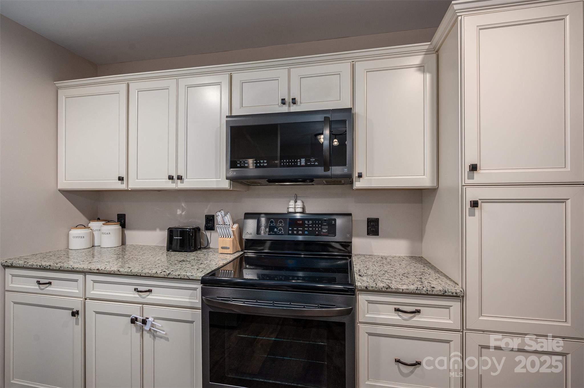 Kitchen with white paneled cabinets, granite countertops, and a black range beneath a microwave.