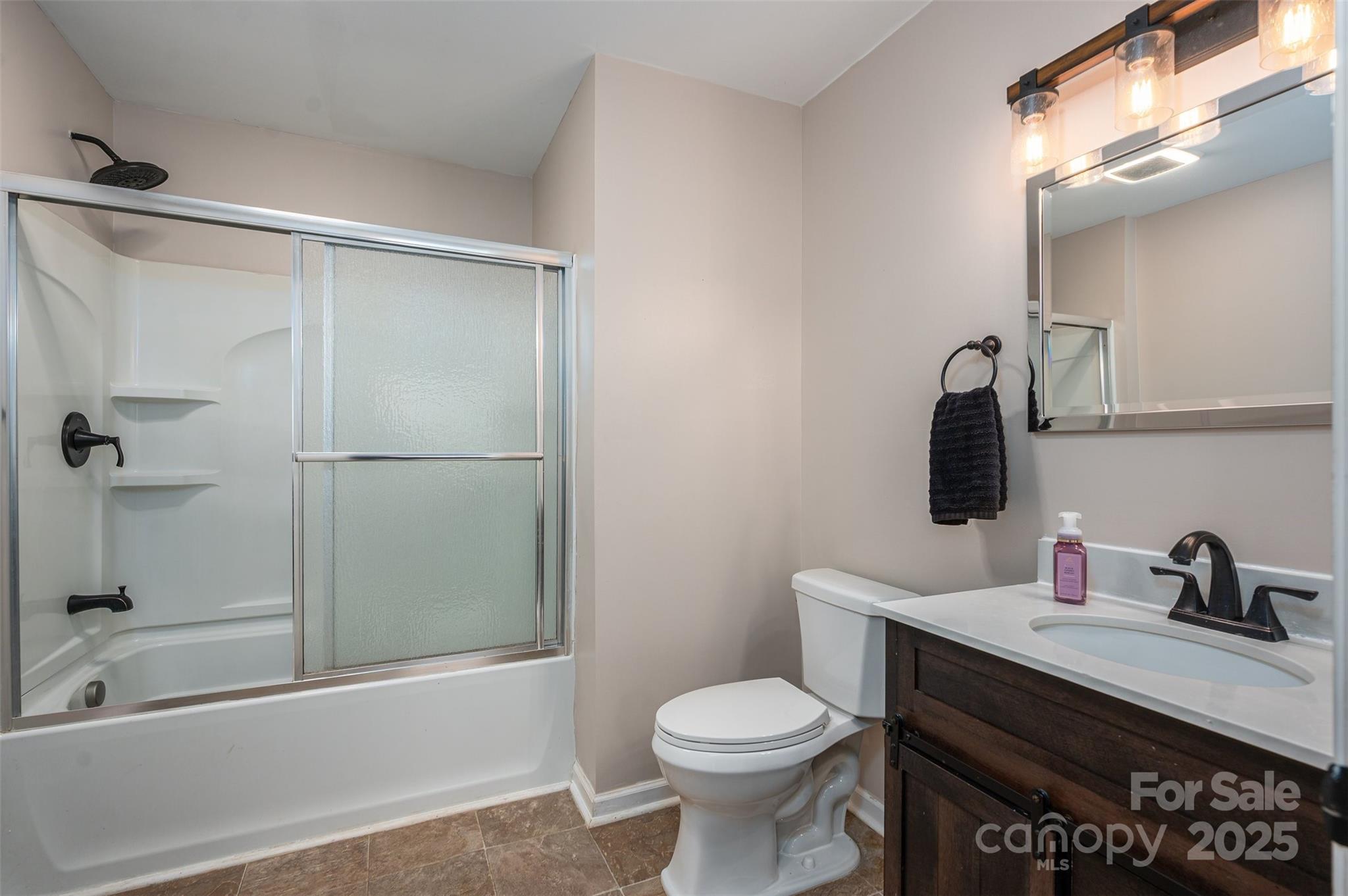 Bathroom with frosted sliding shower doors, a dark wood vanity, and black fixtures.
