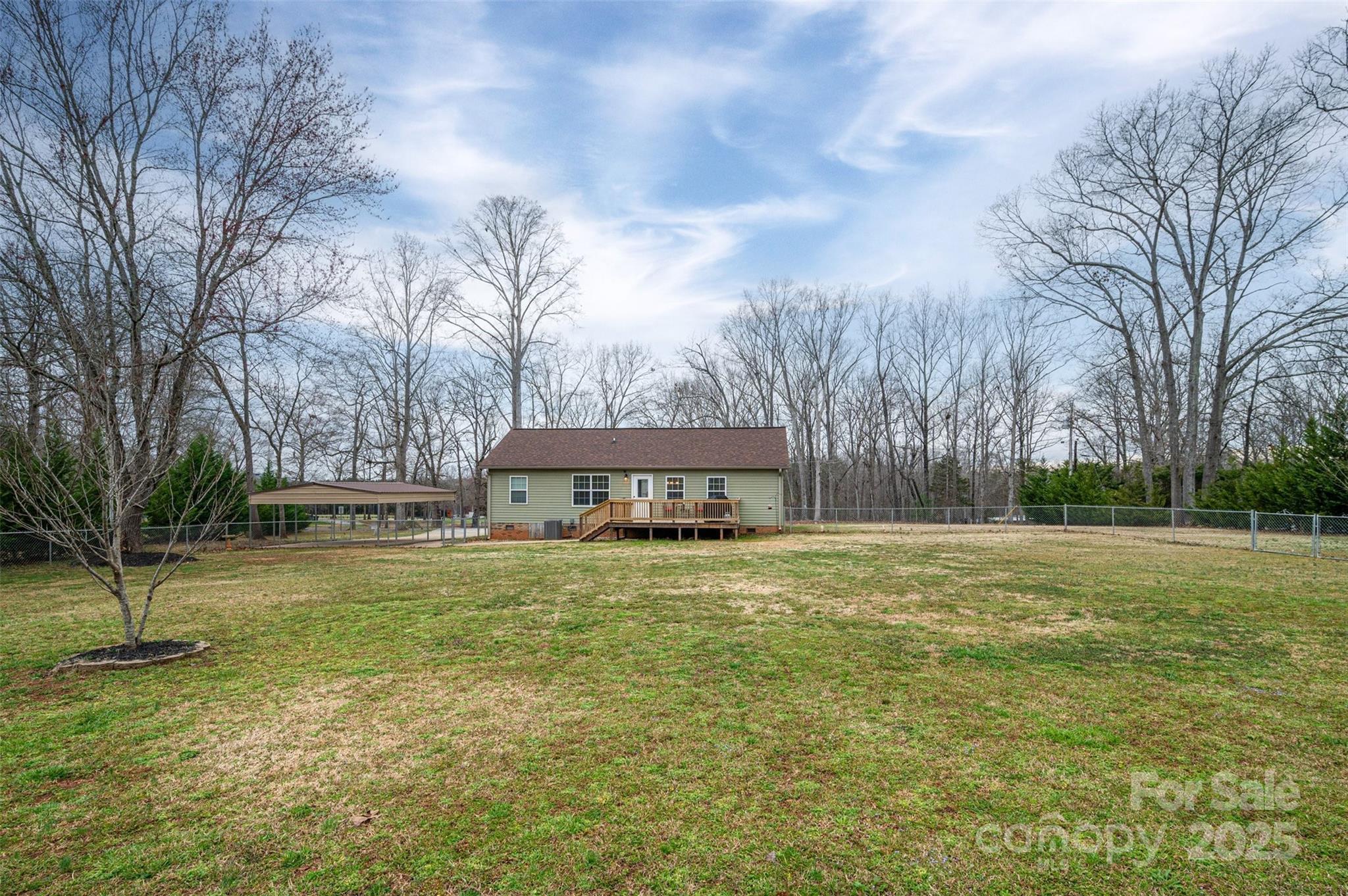Rear of a green single-story house with a wooden deck, carport, and spacious fenced yard.