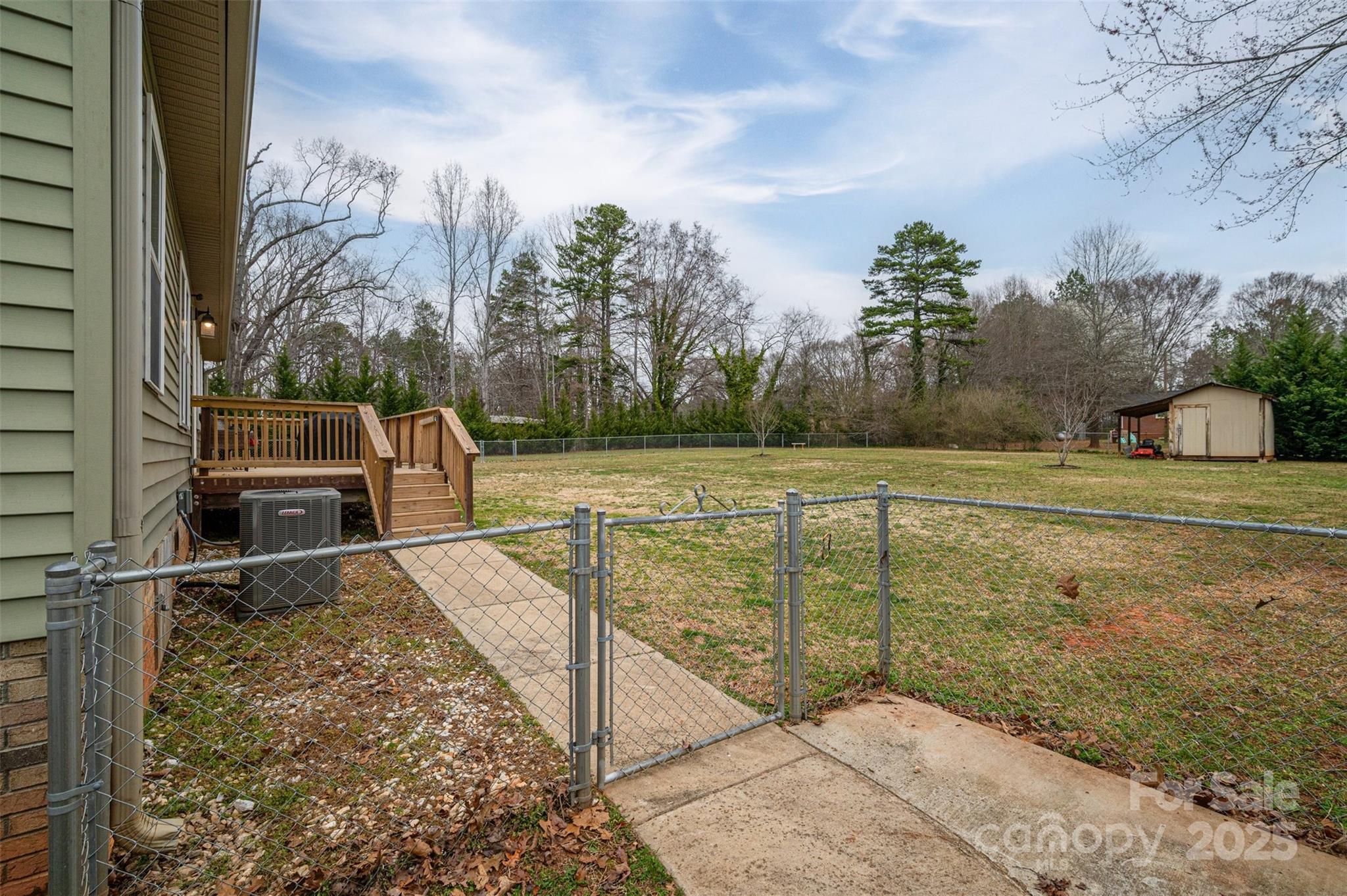 Fenced backyard with a walkway to a wooden deck and a detached shed.