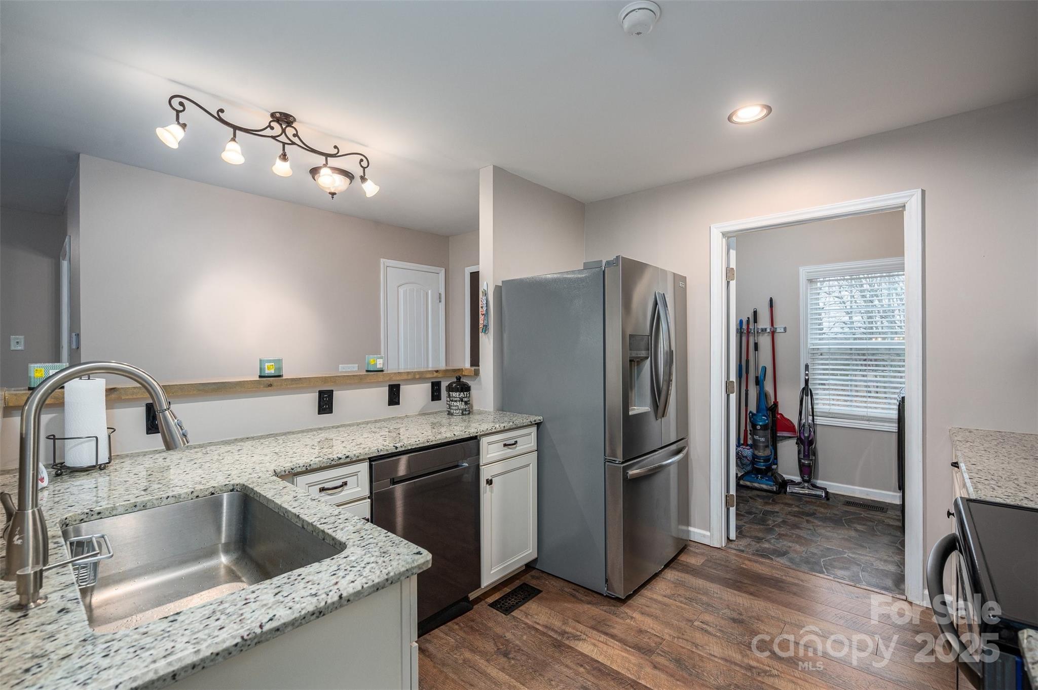 Kitchen with granite counters, stainless-steel appliances, white cabinets, and a doorway to the utility room.
