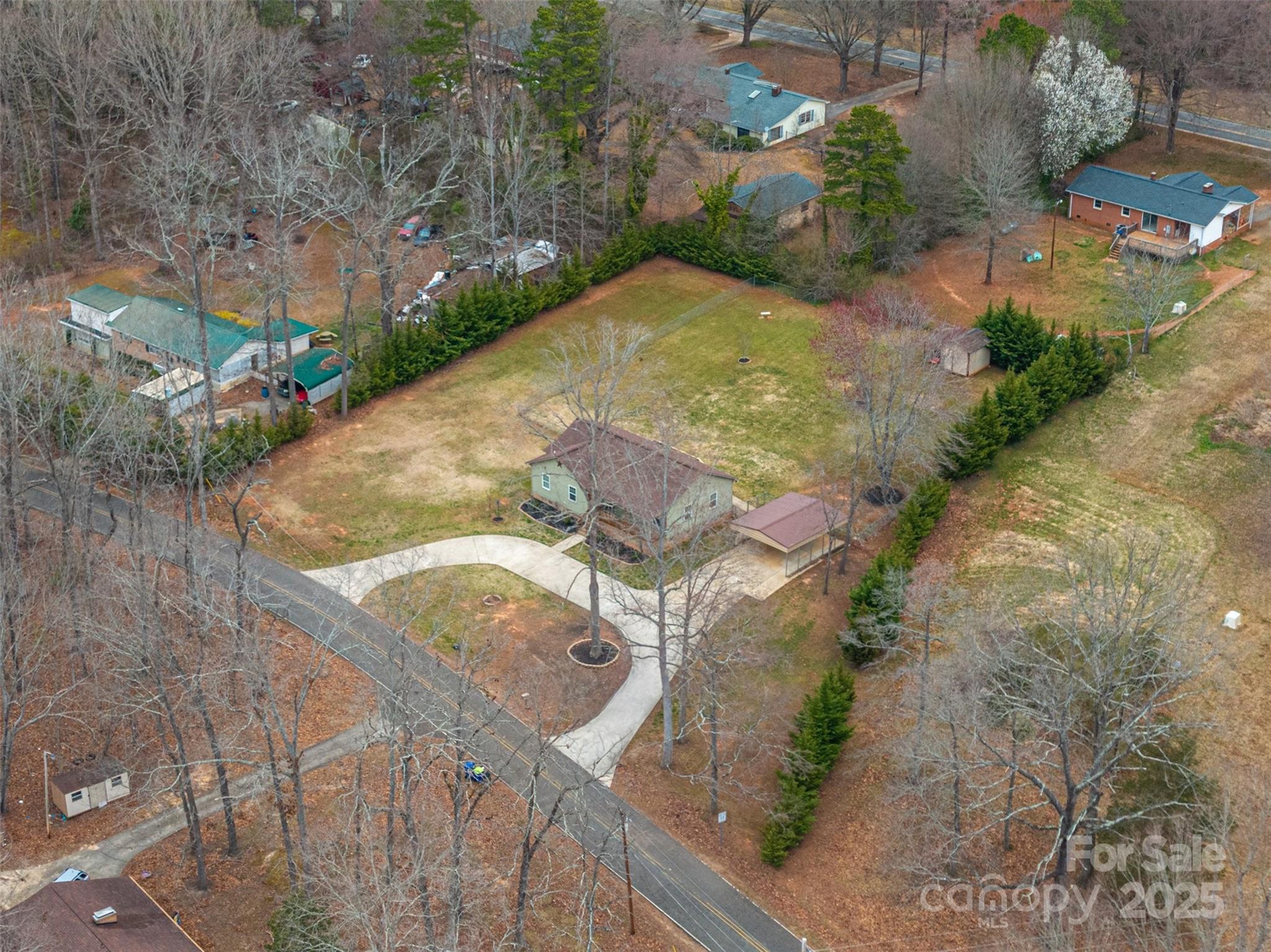 Aerial view of a house on a broad grassy lot with a curved driveway and evergreen borders.
