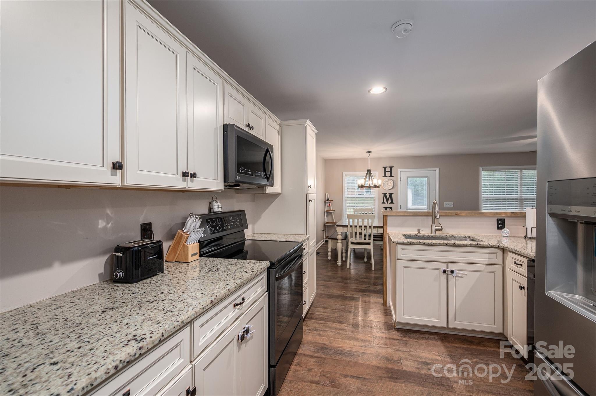 Kitchen with white cabinets, granite countertops, stainless appliances, a central sink island, and dark wood floors.