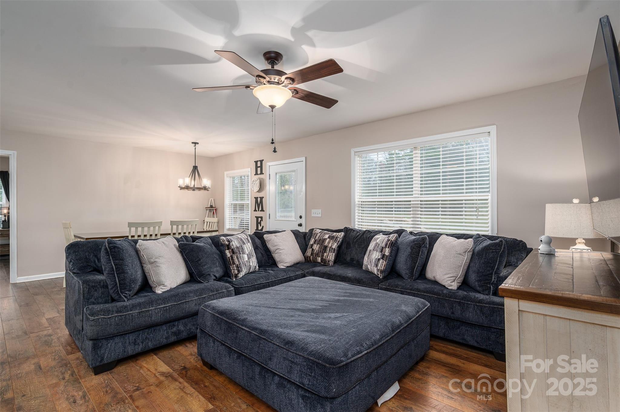 Living room with a dark blue sectional and ottoman, wood flooring, and a dining area behind the sofa.