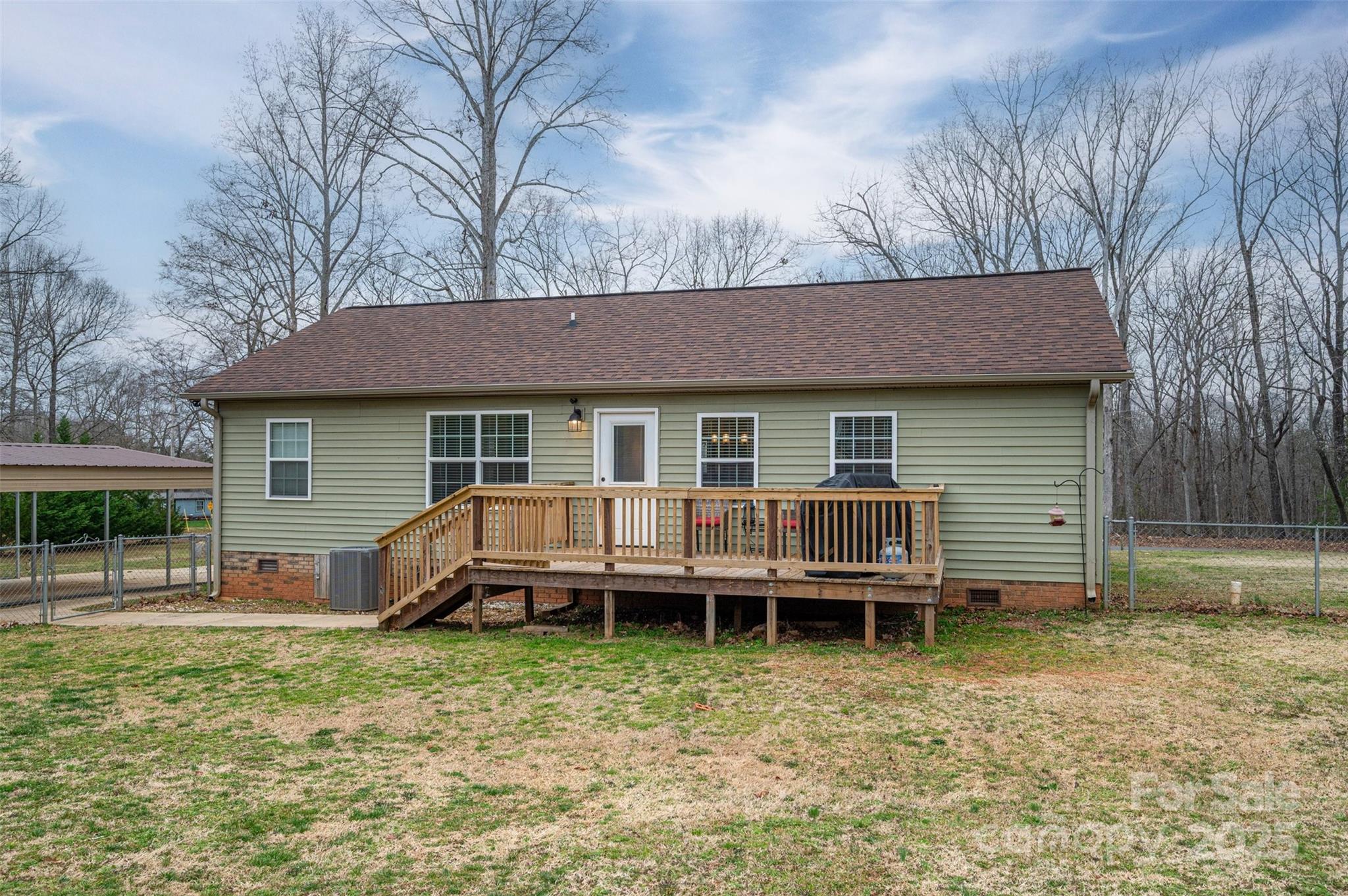 House rear with raised wooden deck, grill, and fenced yard.