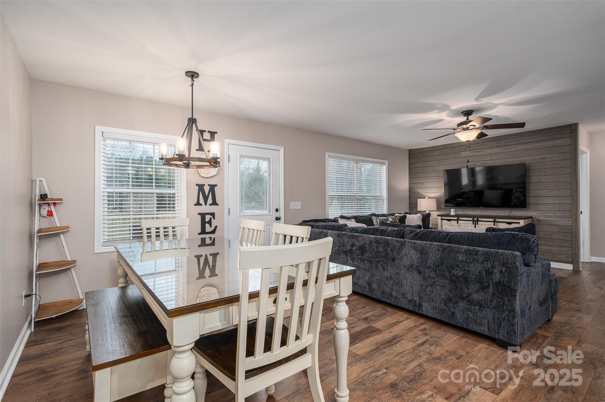 Dining and living room with a glass-top table, dark sectional, and TV on a wood accent wall.