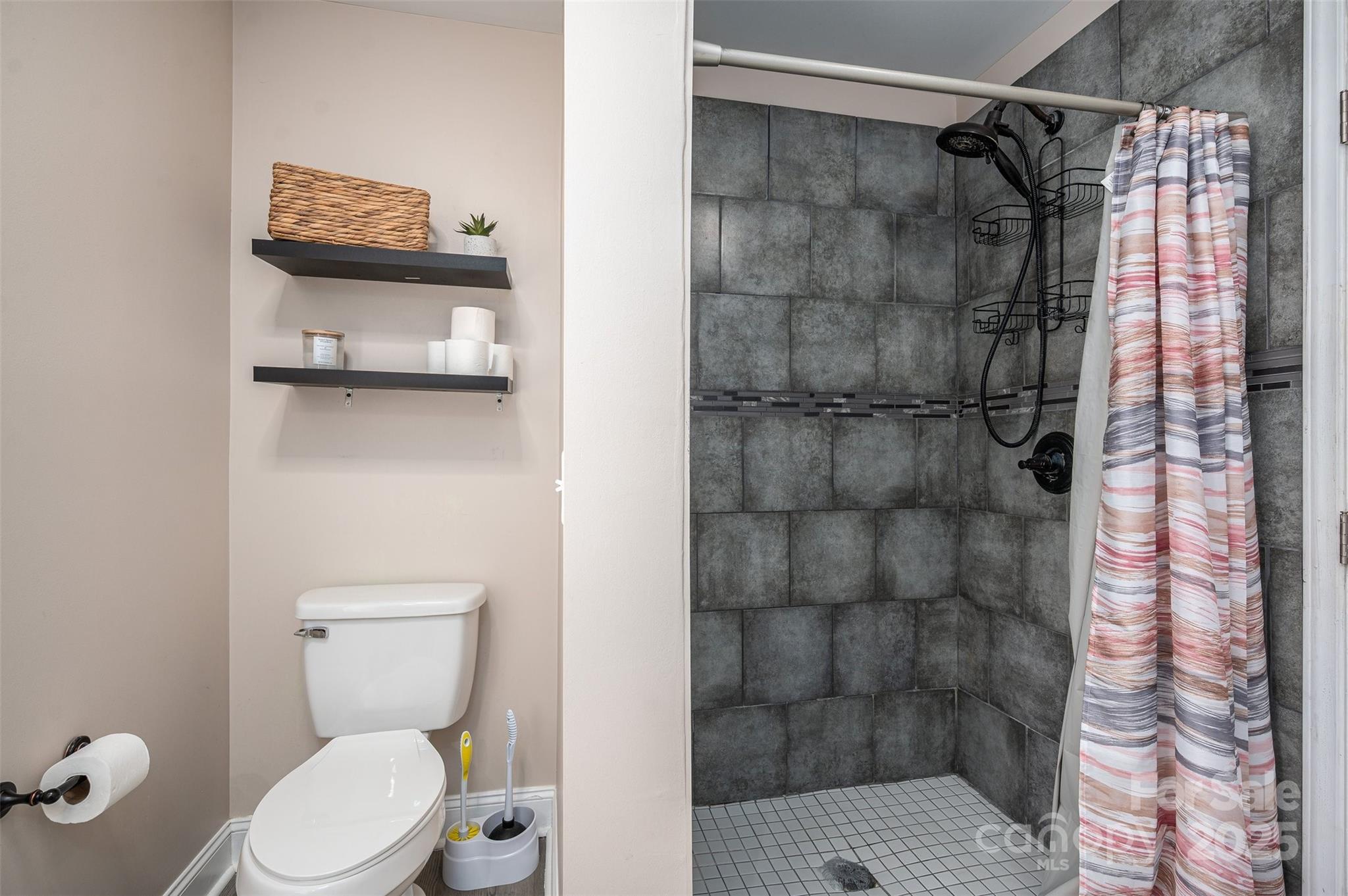 Bathroom with a gray-tiled walk-in shower, black fixtures, and striped curtain beside the toilet.