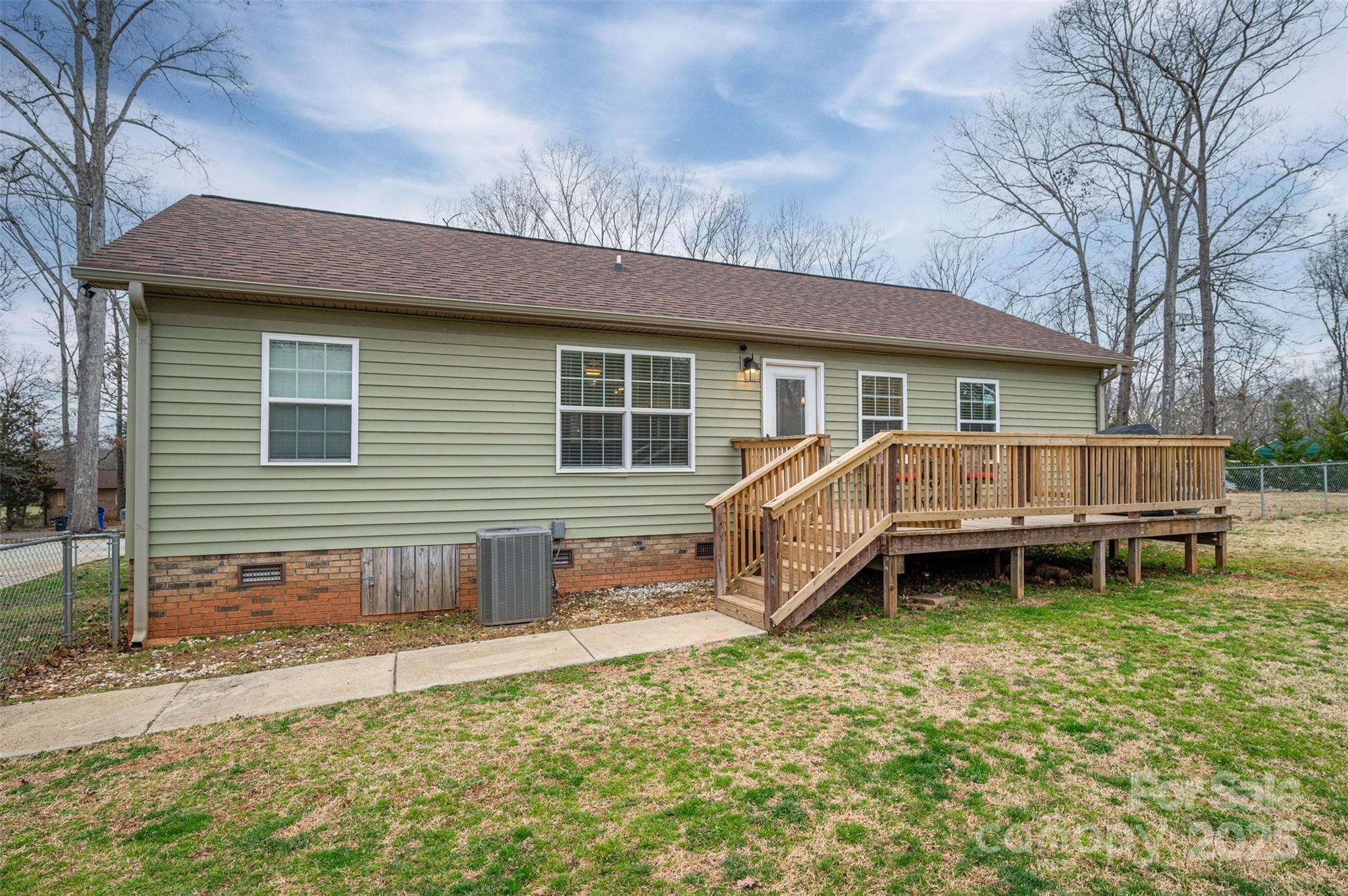 Rear of a pale green home with a raised wooden deck and stairs overlooking a patchy lawn.