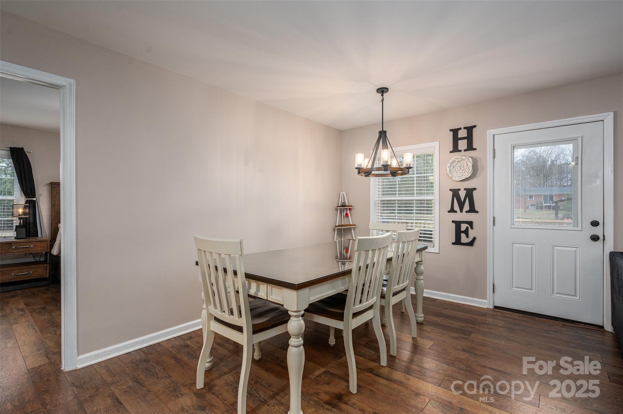 Dining room with white table and chairs, chandelier, and glass-paneled exterior door.
