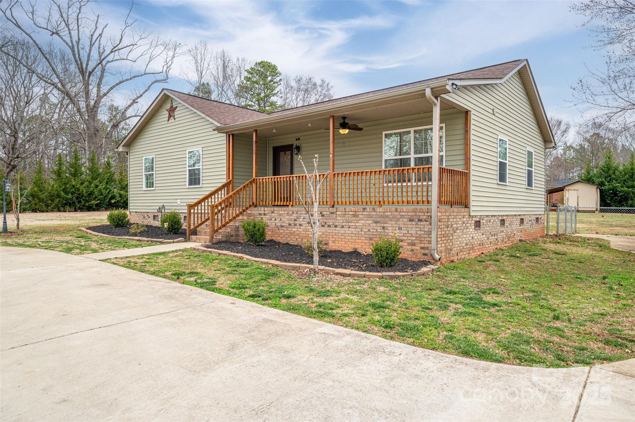 Single-story green-sided home with a brick foundation and a covered wooden front porch.
