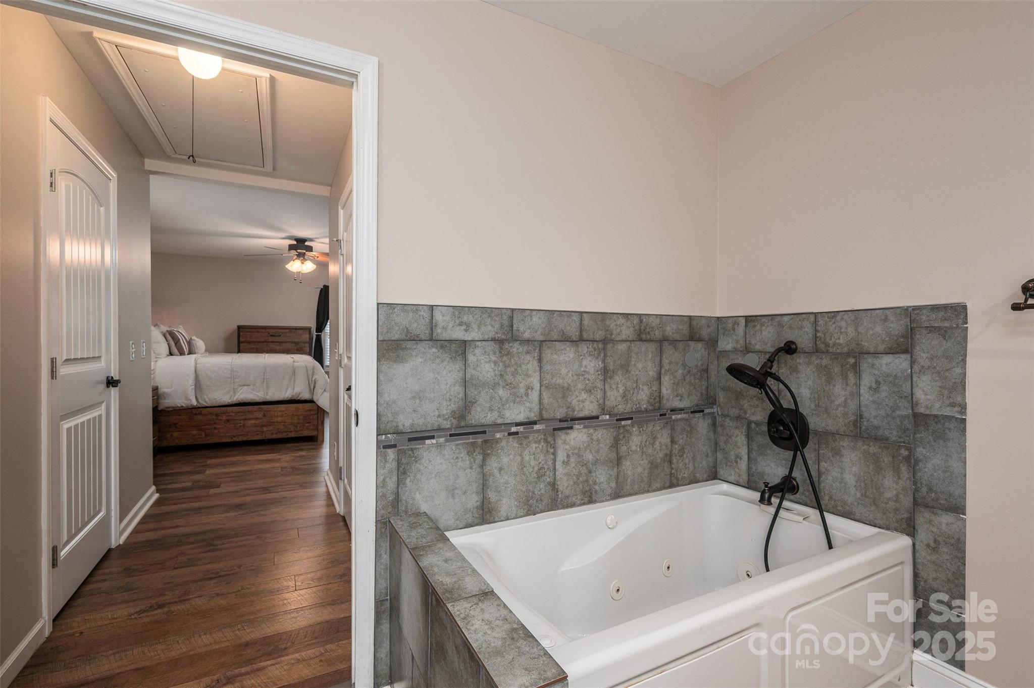 Bathroom with a large jetted tub and gray tile, opening onto a furnished bedroom.
