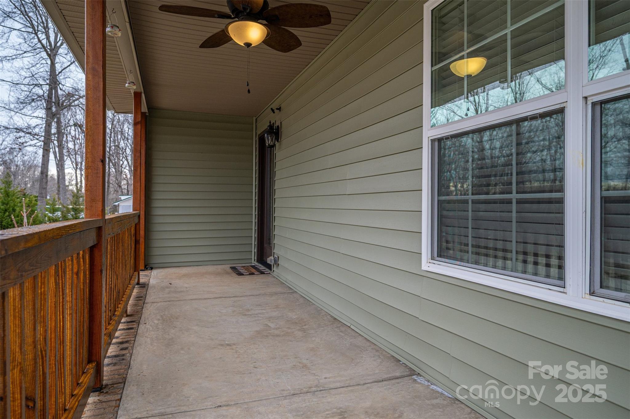Covered concrete porch with wood railing, green siding, large windows, and a ceiling fan.