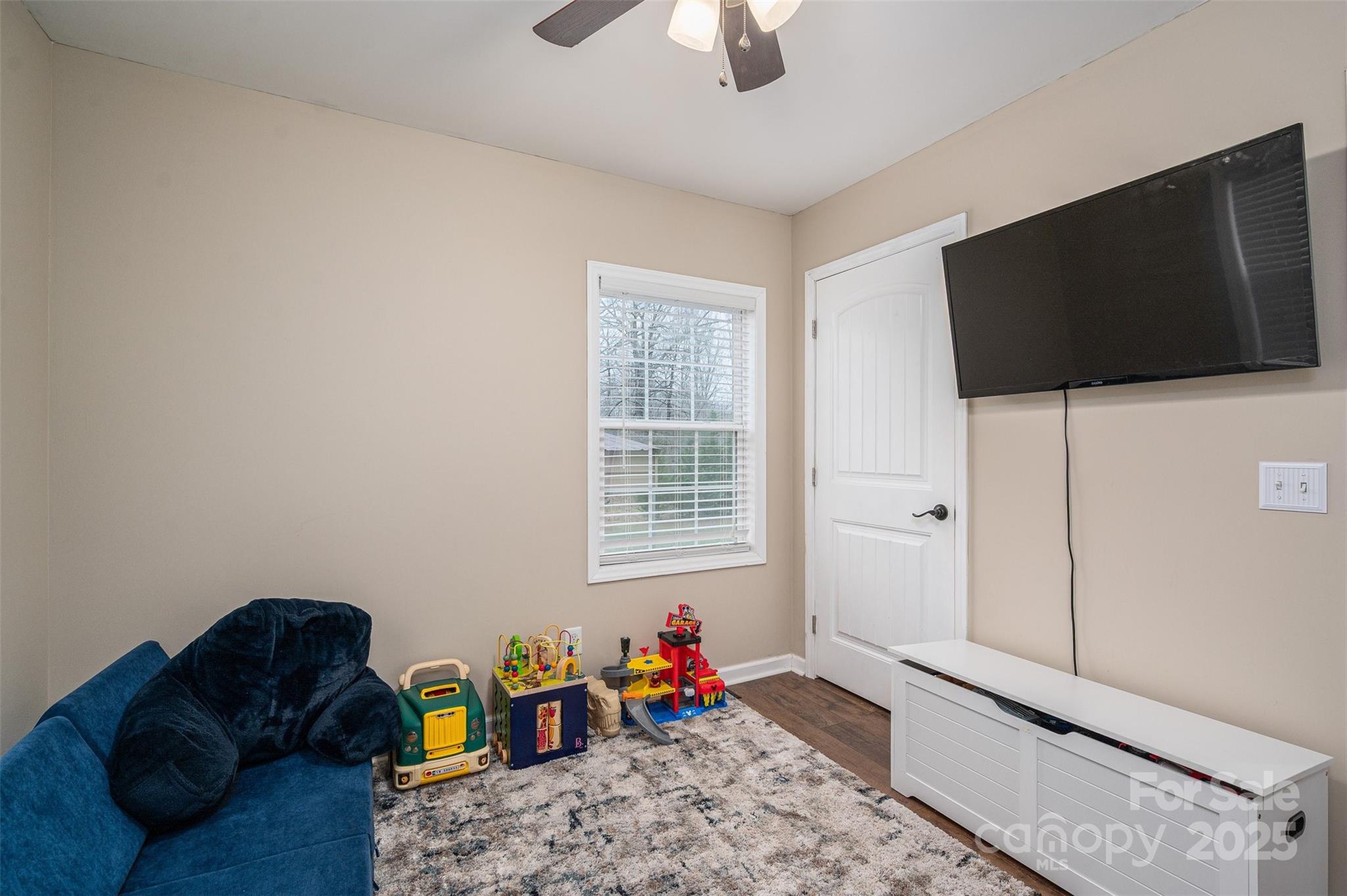 Playroom with children's toys, a blue chair, patterned rug, and wall-mounted television.