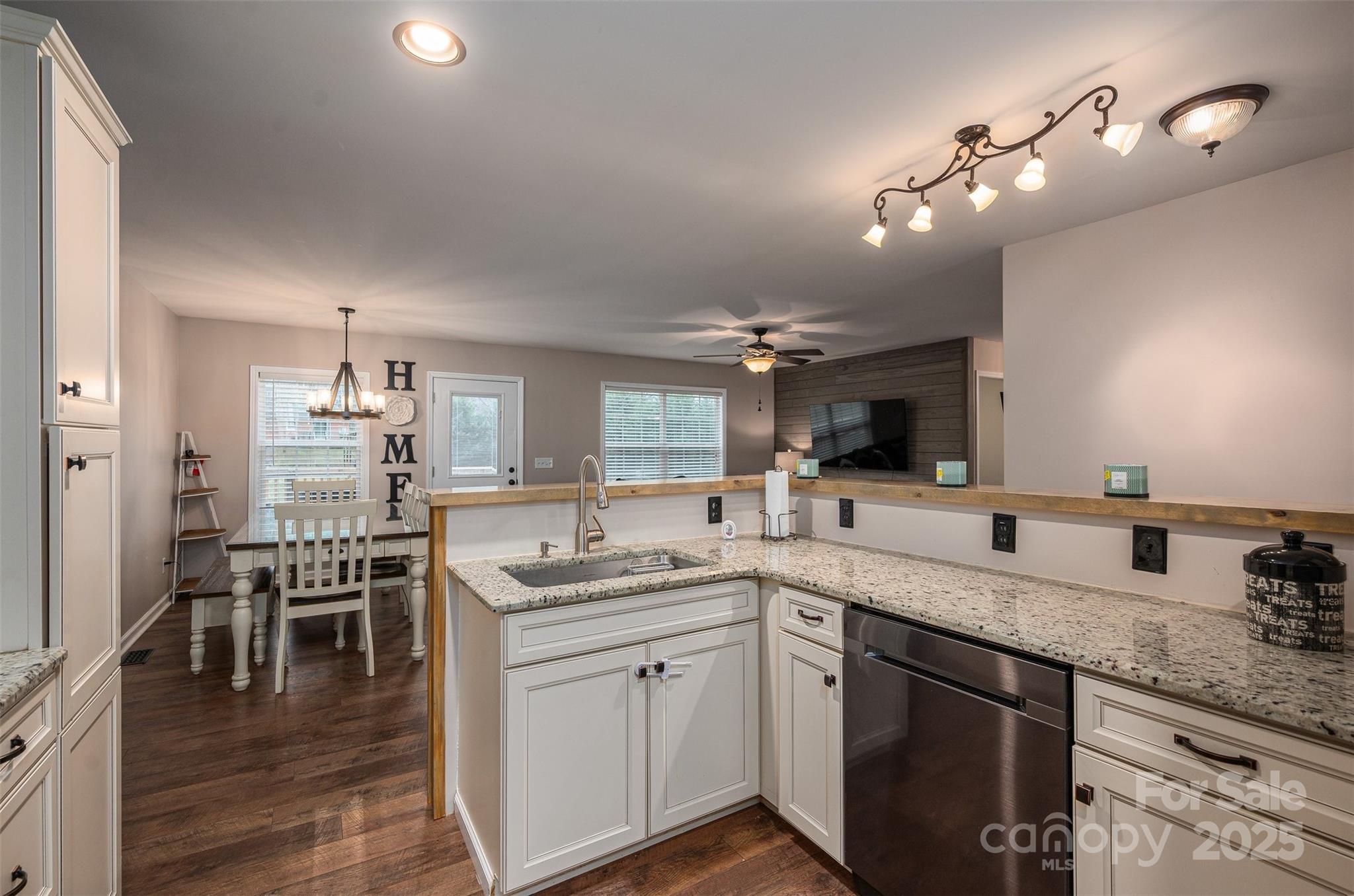 Open-plan kitchen with white cabinets, granite counters, stainless dishwasher, and a dining area beyond.