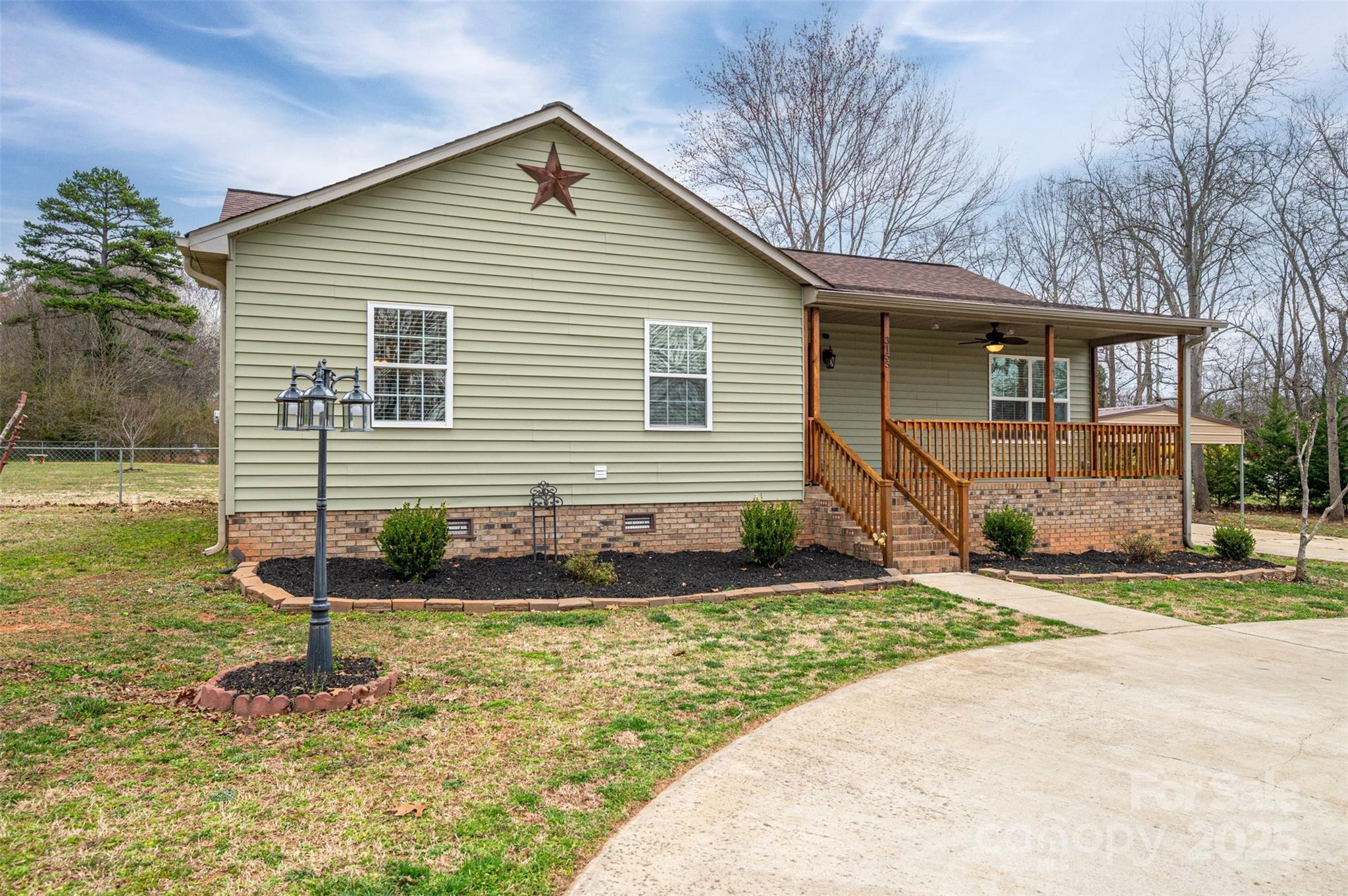 Sage-sided home with a brick foundation, covered wooden porch, and star on the front gable.