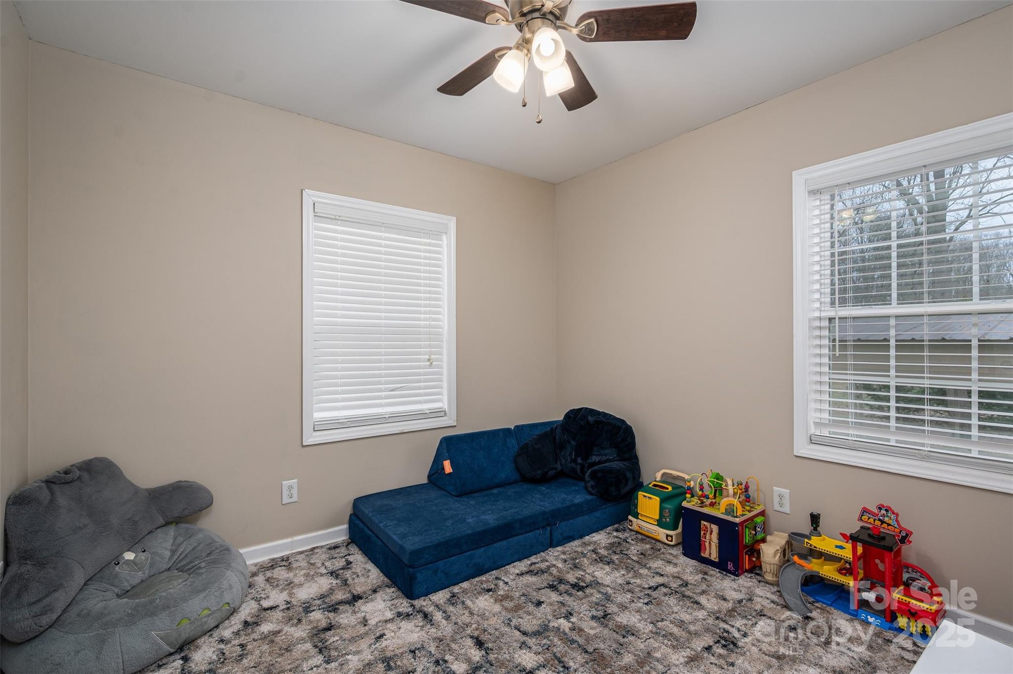 Children’s playroom with a blue chaise sofa, toys, two windows, and a ceiling fan.