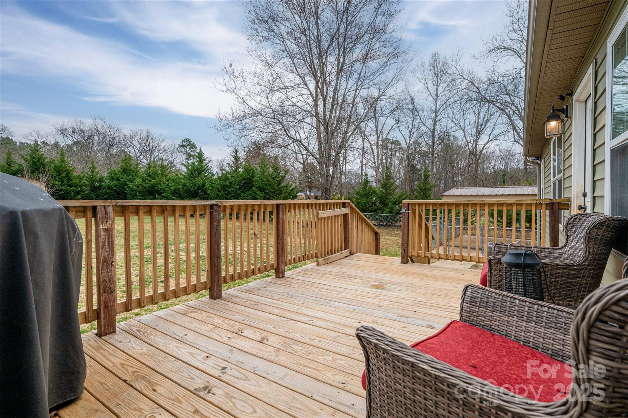 Wooden backyard deck with wicker seating, red cushions, and railings overlooking a lawn and trees.
