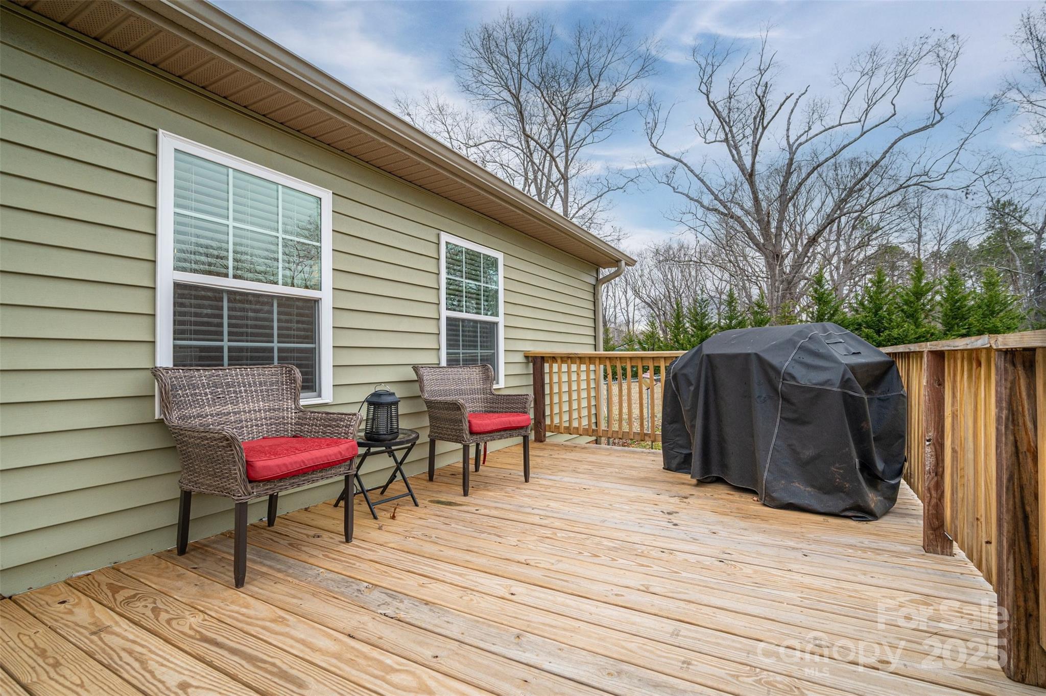 Wooden deck with red-cushioned wicker chairs, a covered grill, and a wood privacy fence.