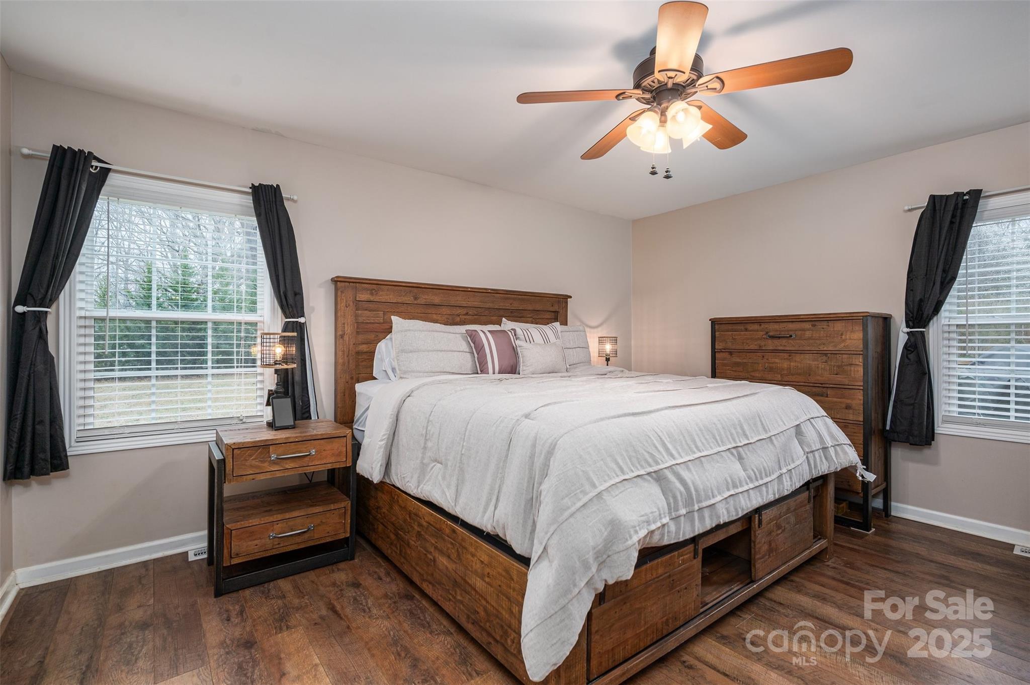 Furnished bedroom with a rustic wood bed, white bedding, matching dresser, and windows with dark curtains.