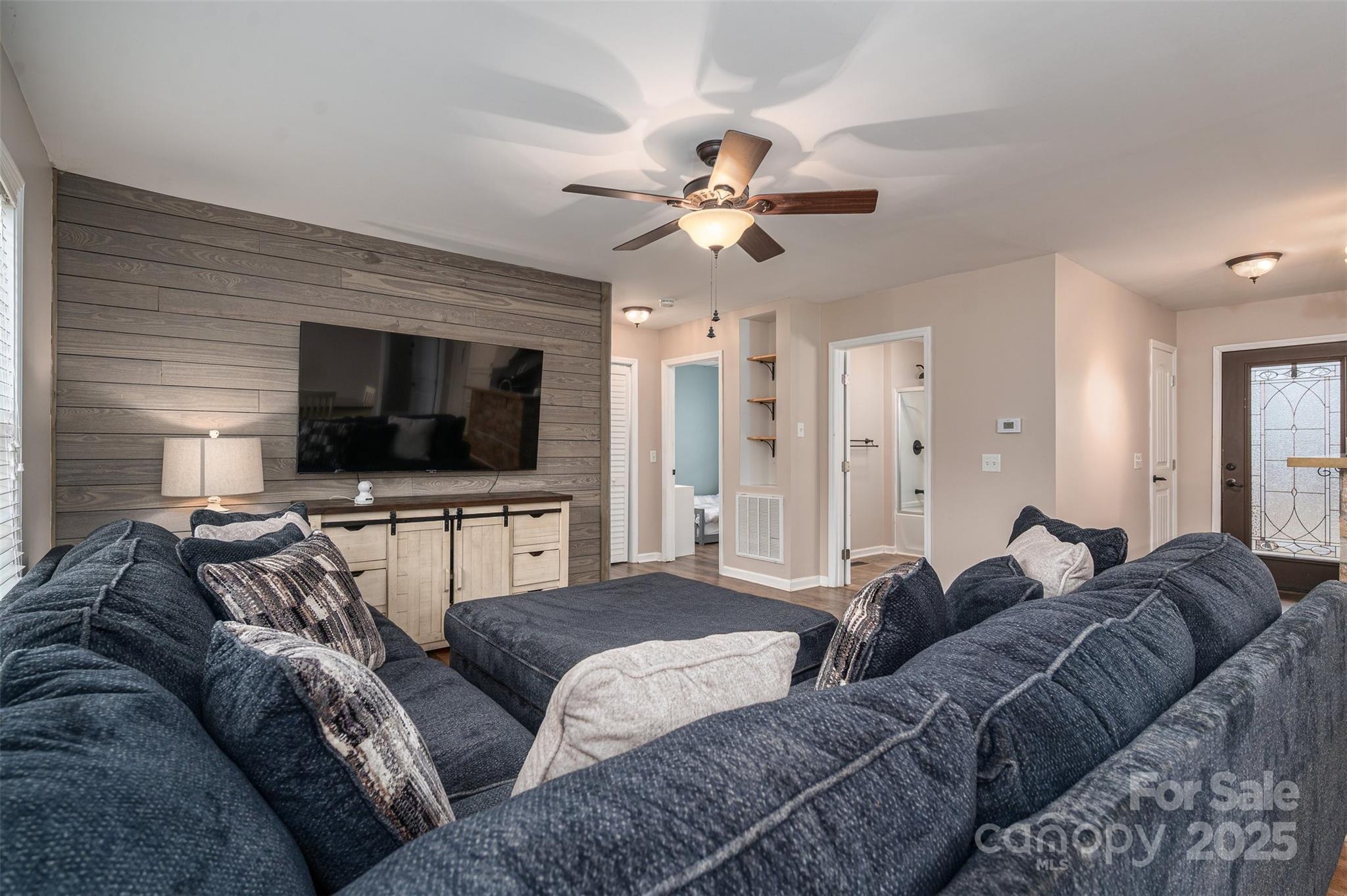 Living room with a large dark sectional, ceiling fan, and television on a gray wood accent wall.