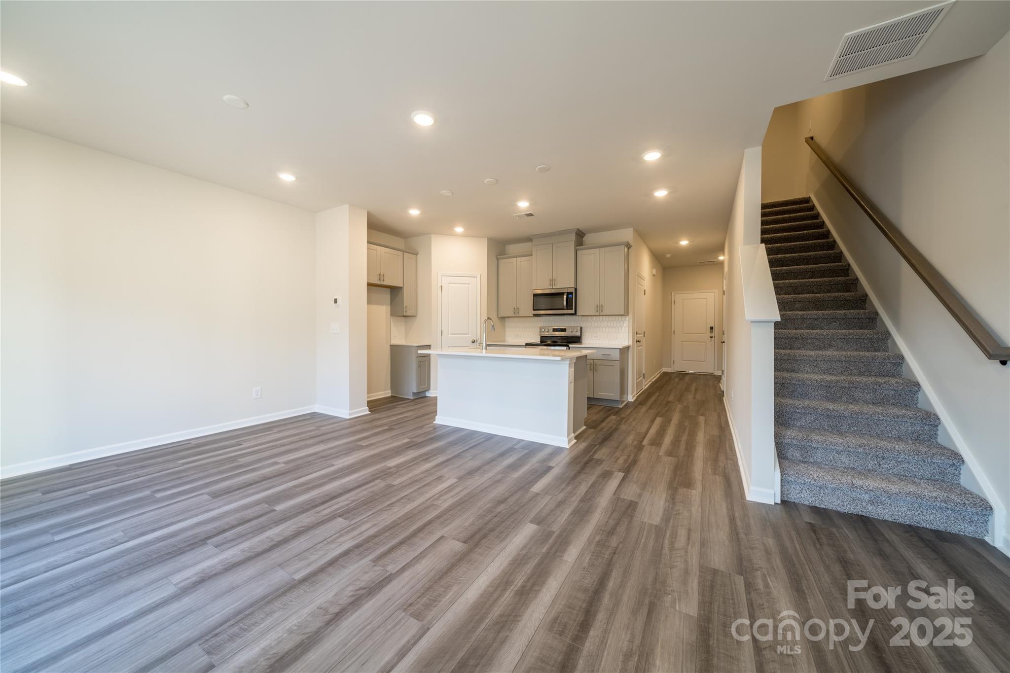 Open kitchen and living area with a white island, gray flooring, and carpeted stairs.