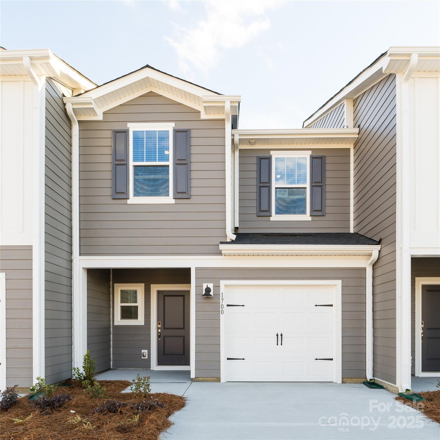Gray two-story home with white trim, dark shutters, and a white garage door.