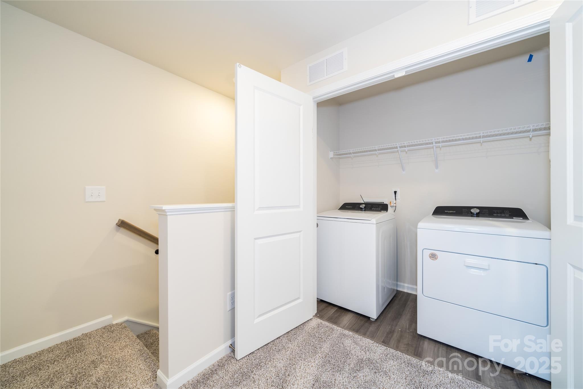 Laundry room with white washer and dryer beneath wire shelving, viewed from an open doorway.