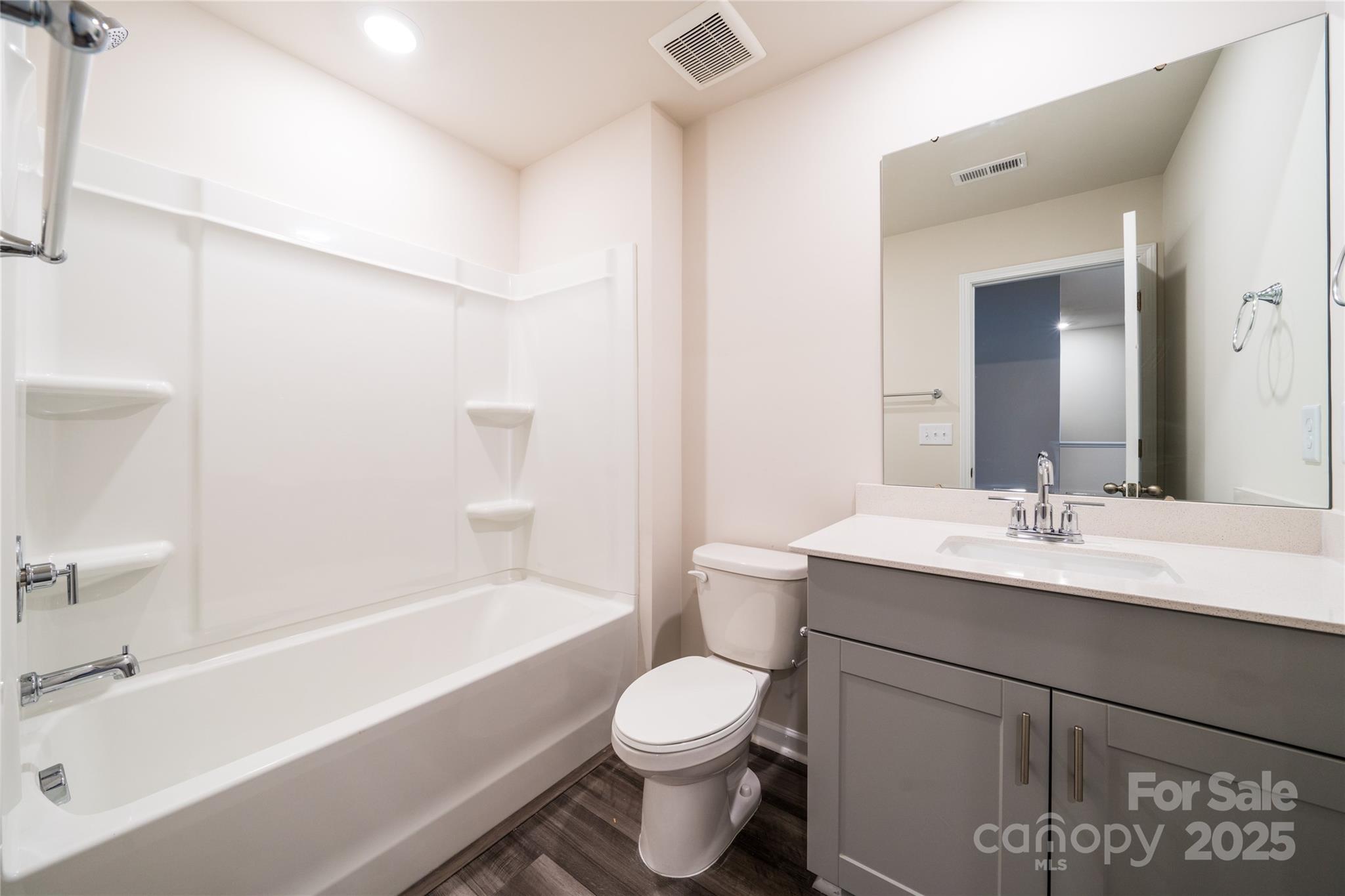 Bathroom with a white tub and shower, gray vanity, toilet, and large mirror.