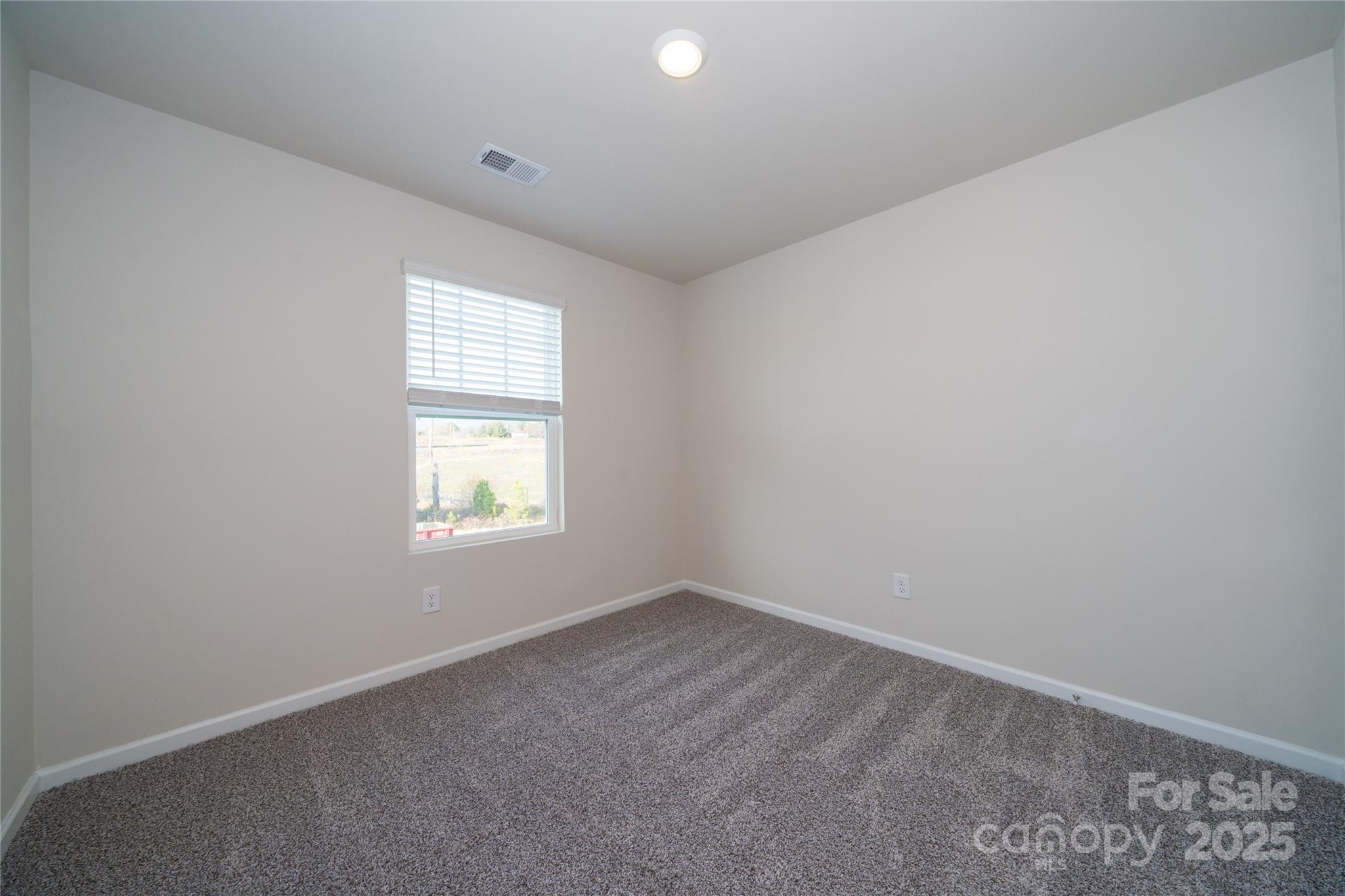 Empty carpeted bedroom with neutral walls and a window fitted with white blinds.