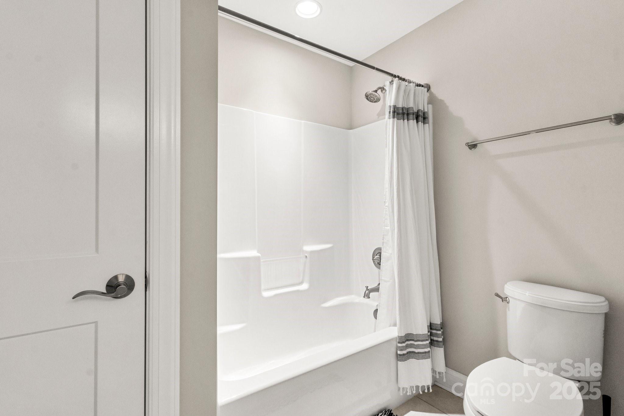 Bathroom with a white tub and shower, striped curtain, and toilet.
