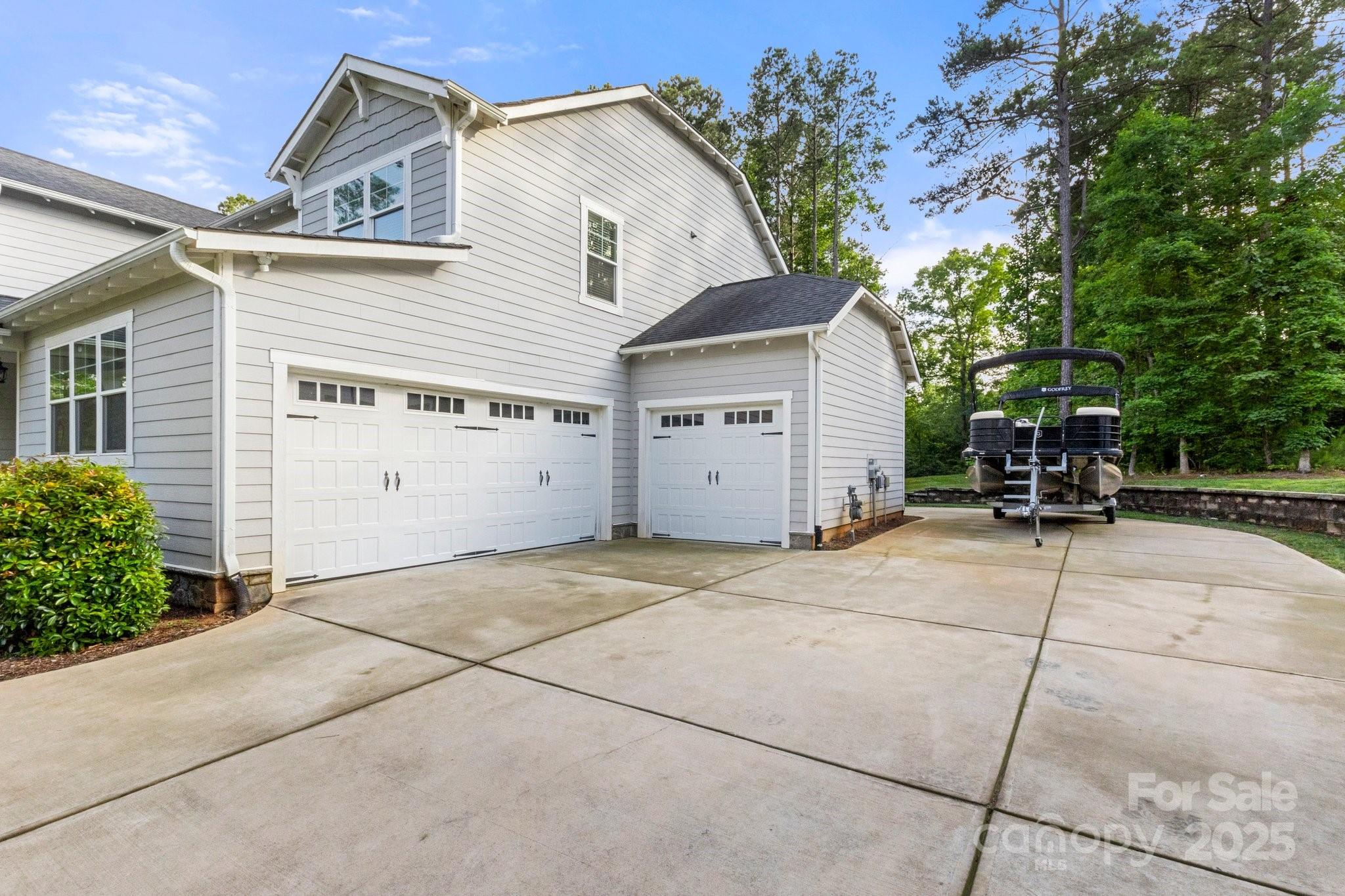 Gray two-story house with two garages and a pontoon boat parked on the wide driveway.