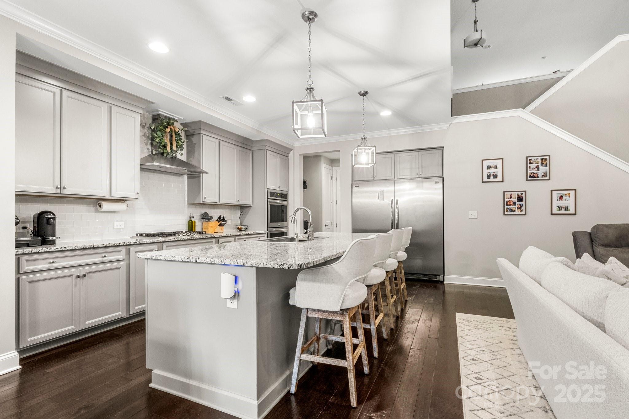Kitchen with gray cabinetry, stainless steel appliances, and a large granite island with bar stools.