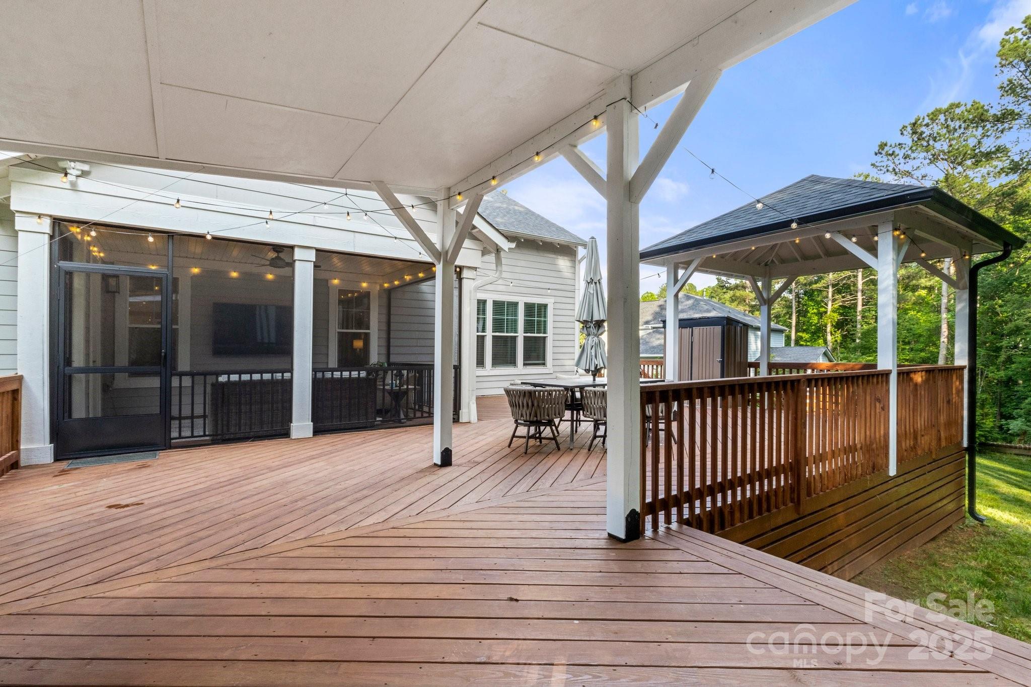 Covered wooden deck with screened porch, dining set, string lights, and a gazebo.