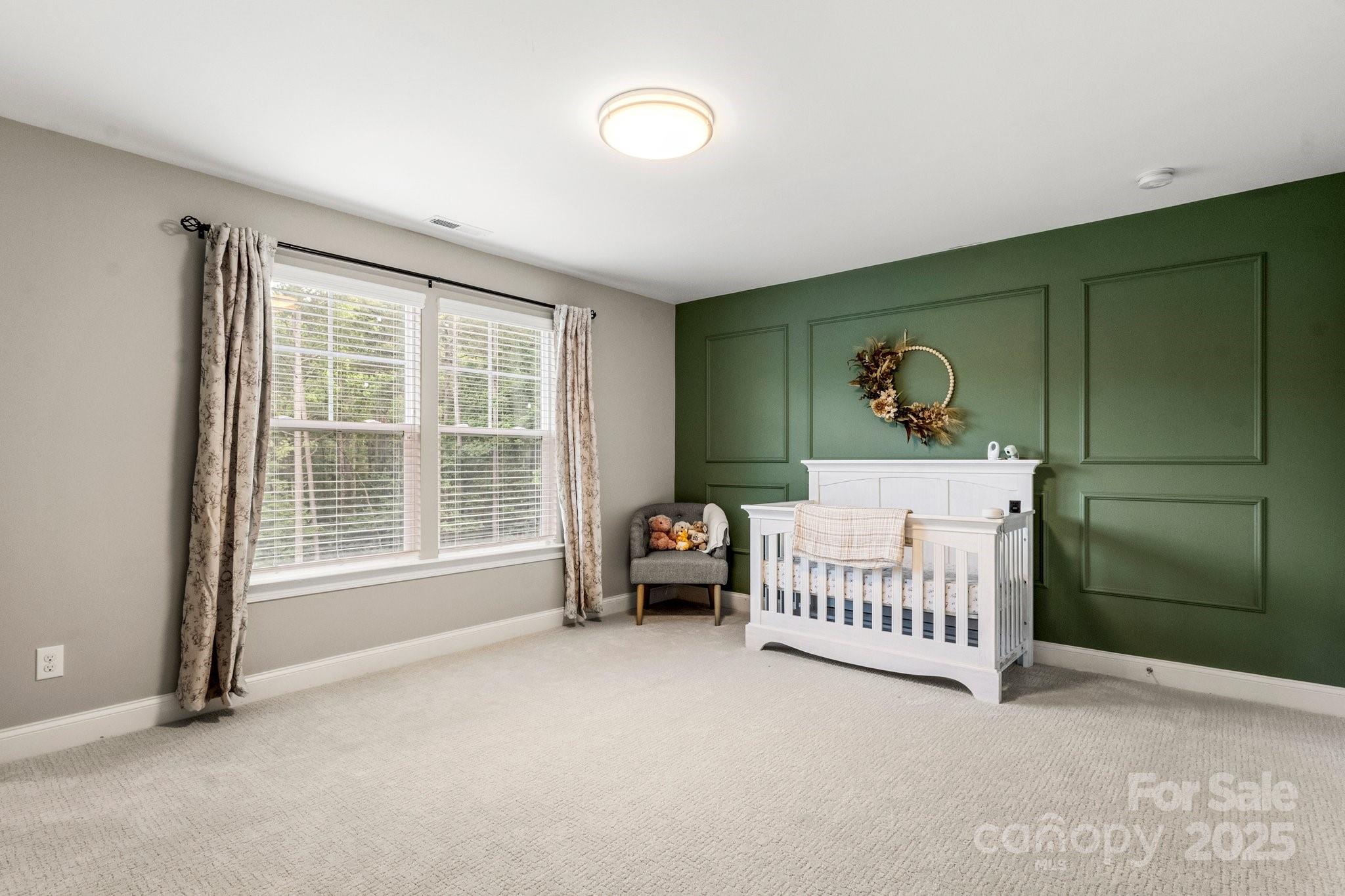Nursery with a white crib, dark green paneled wall, and two large windows.