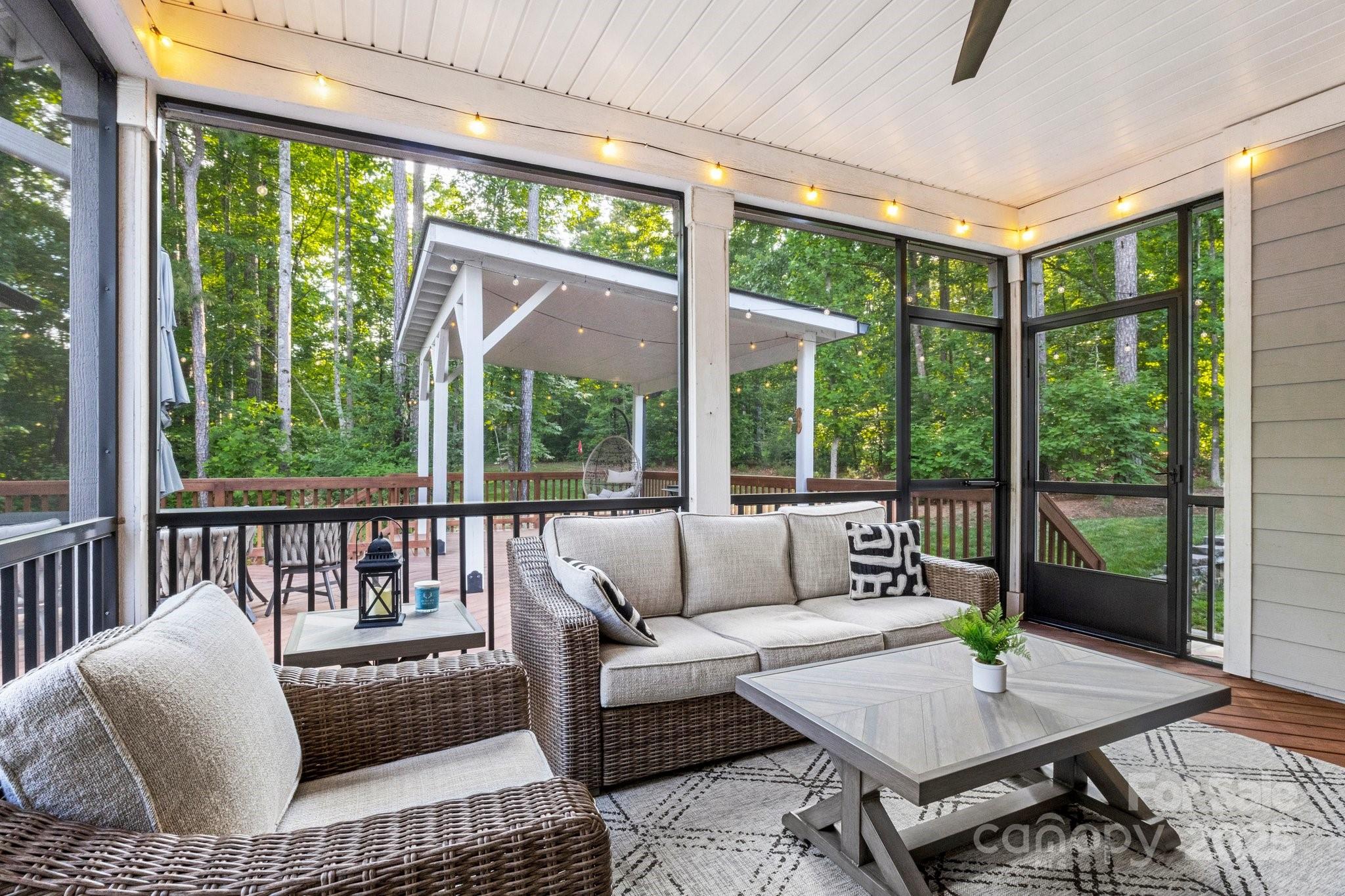 Screened porch with wicker seating and string lights overlooking a wooded yard.