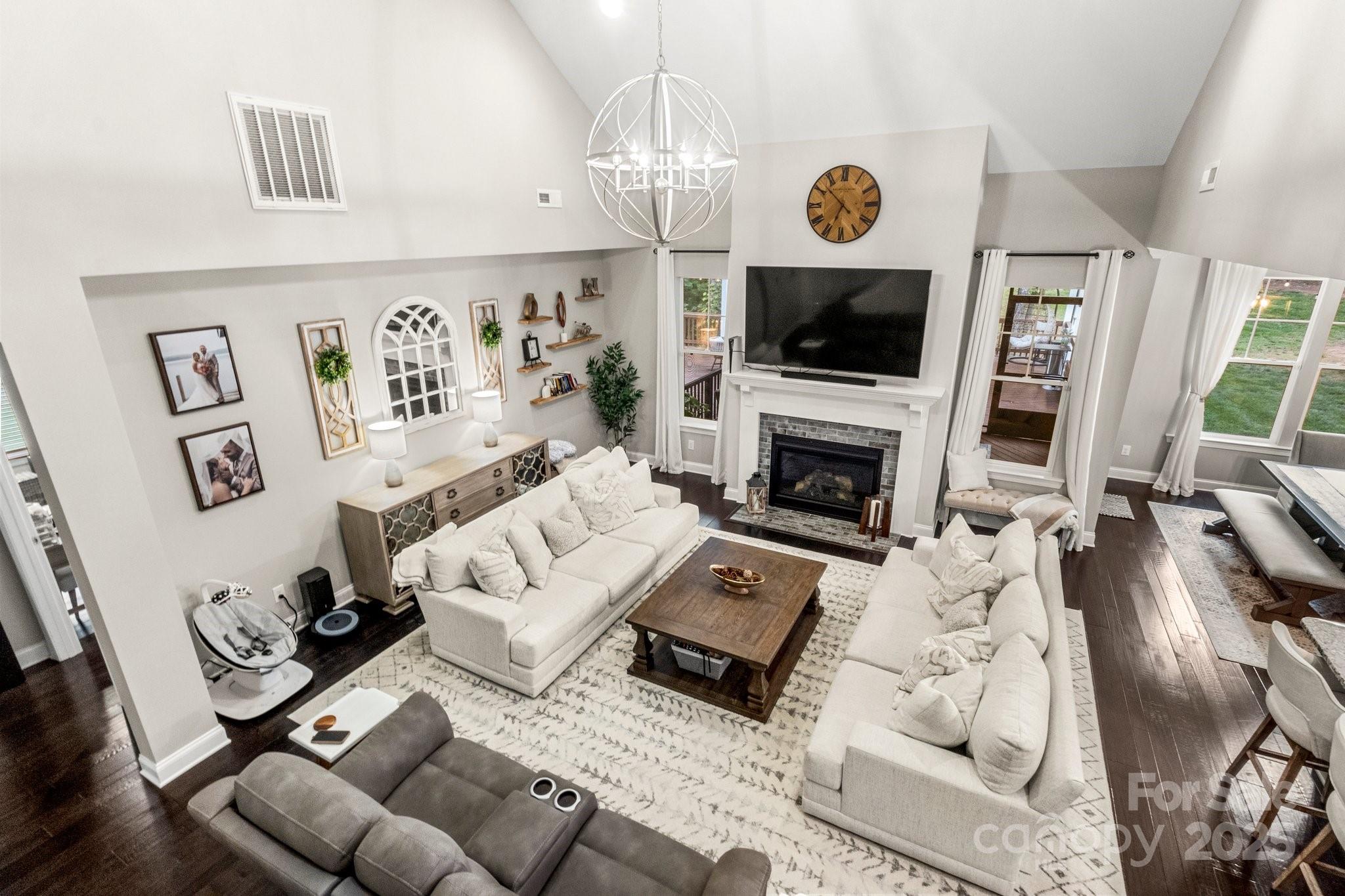 Vaulted living room with cream sofas, a fireplace, and a television above the mantel.