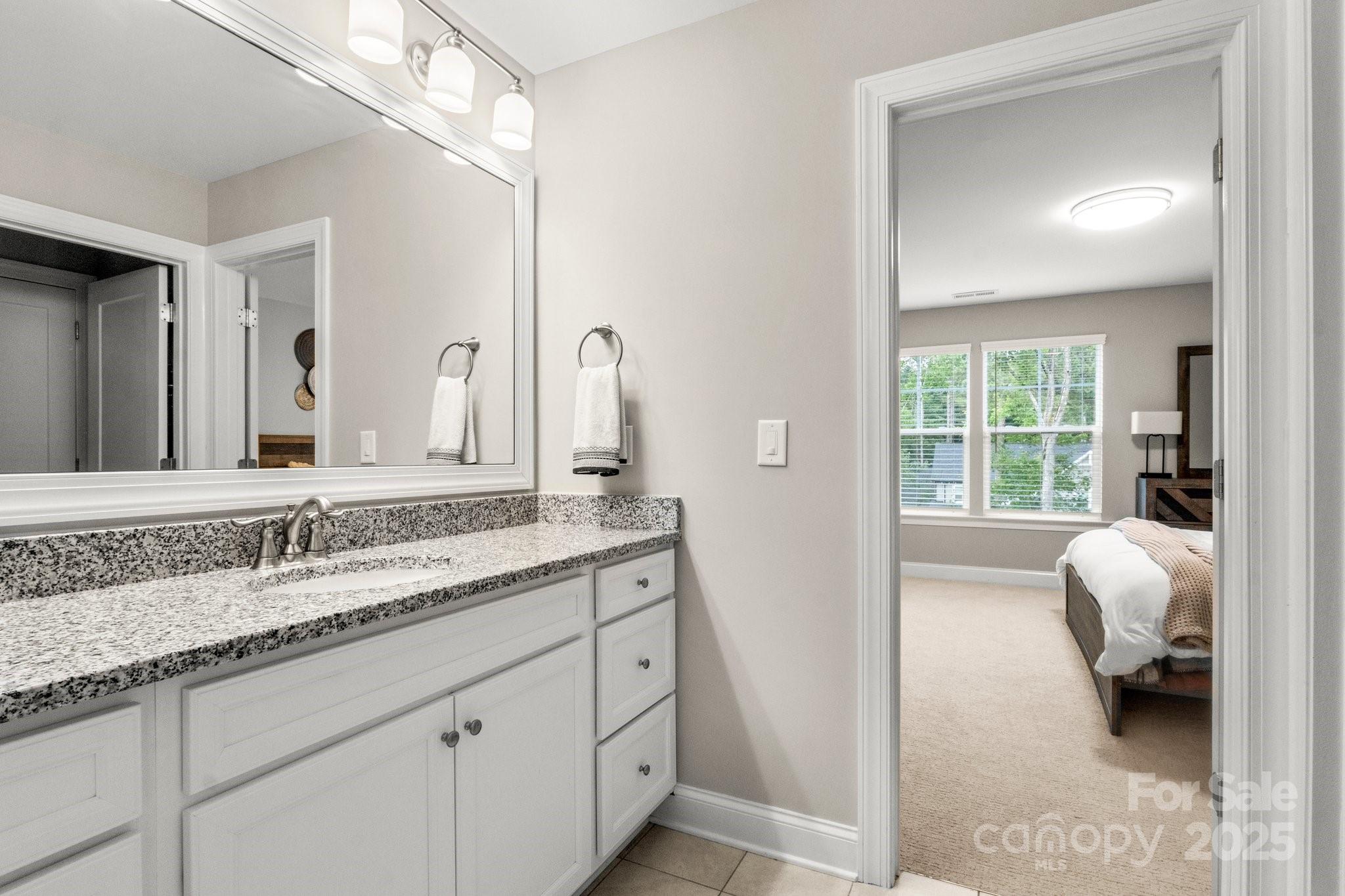 Bathroom vanity with granite countertop and mirror, looking through a doorway into a furnished bedroom.