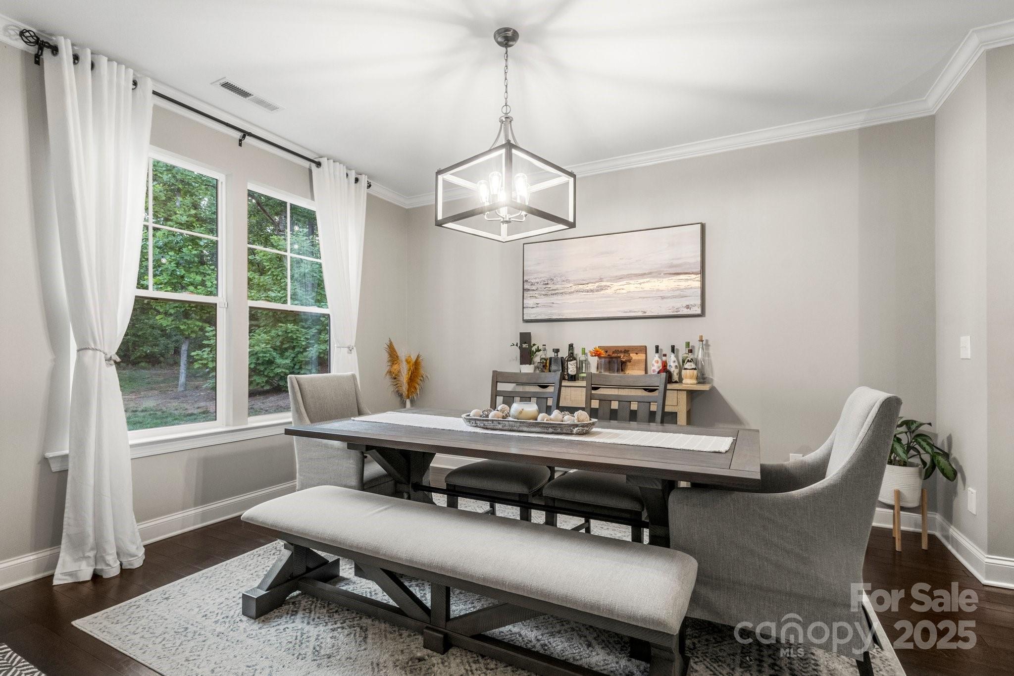 Dining room with a dark wood table, upholstered seating, geometric pendant light, and large windows overlooking trees.