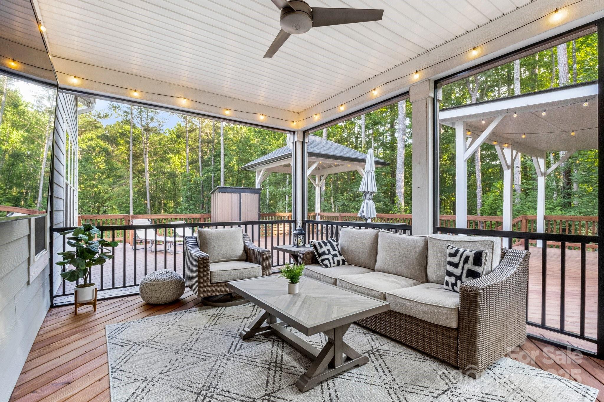 Covered porch with wicker seating and string lights overlooking a wooded deck and gazebo.