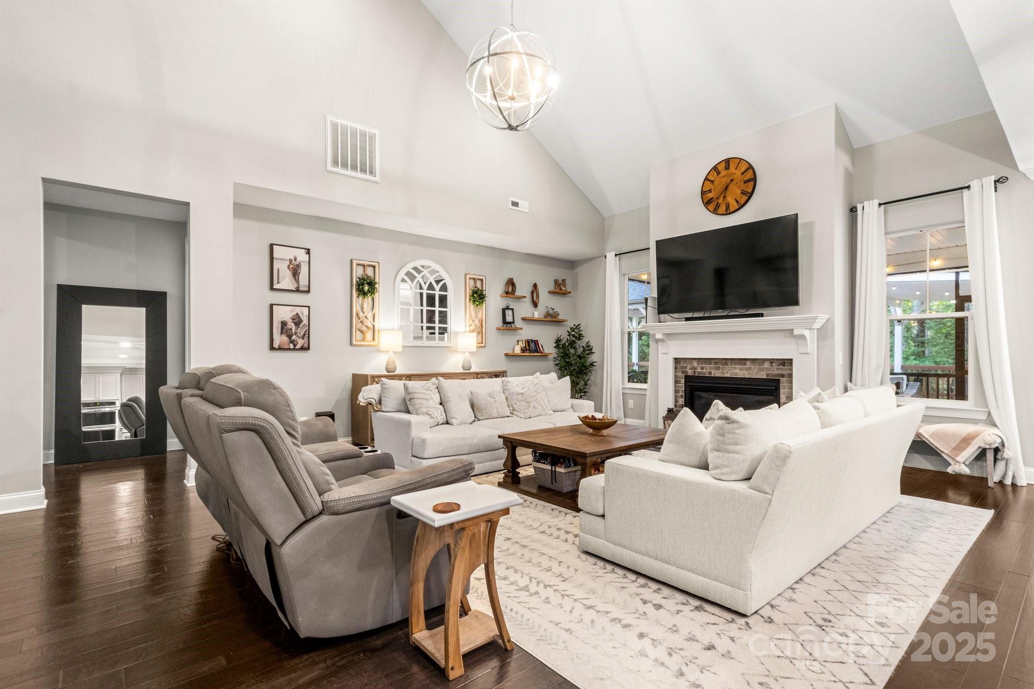 Vaulted living room with white sofas, gray recliners, and a fireplace beneath a wall-mounted television.