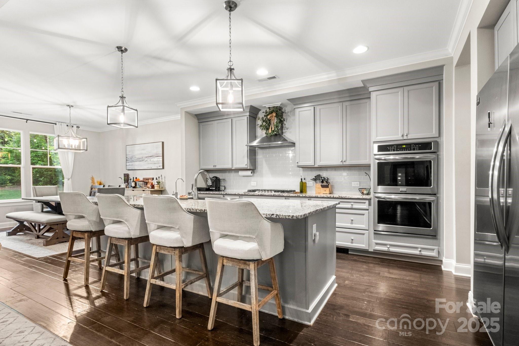 Kitchen with a large granite island, gray cabinetry, stainless appliances, and adjoining dining area.