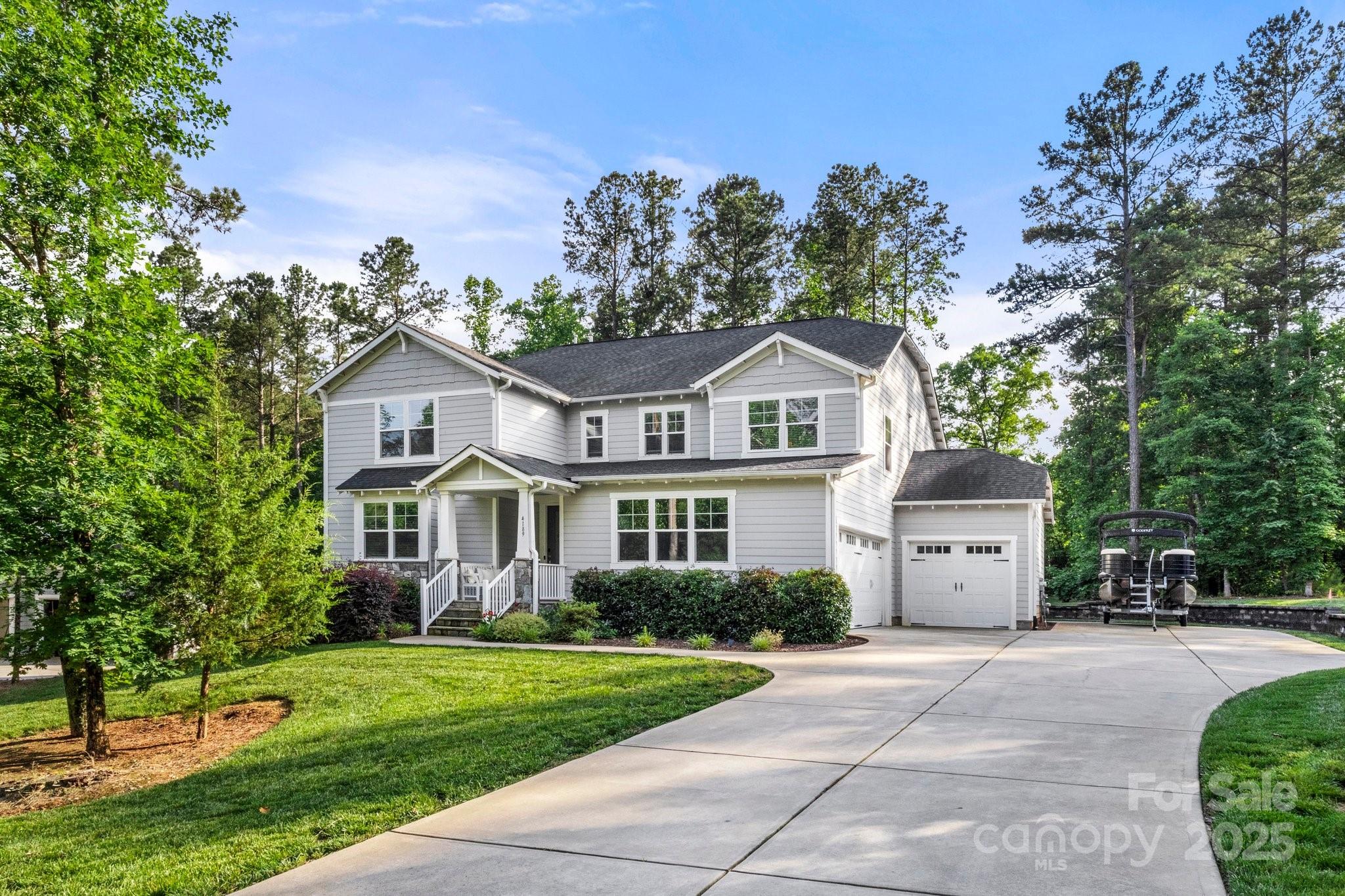 Gray two-story house with white trim, multiple garages, a curved driveway, and a boat parked beside it.