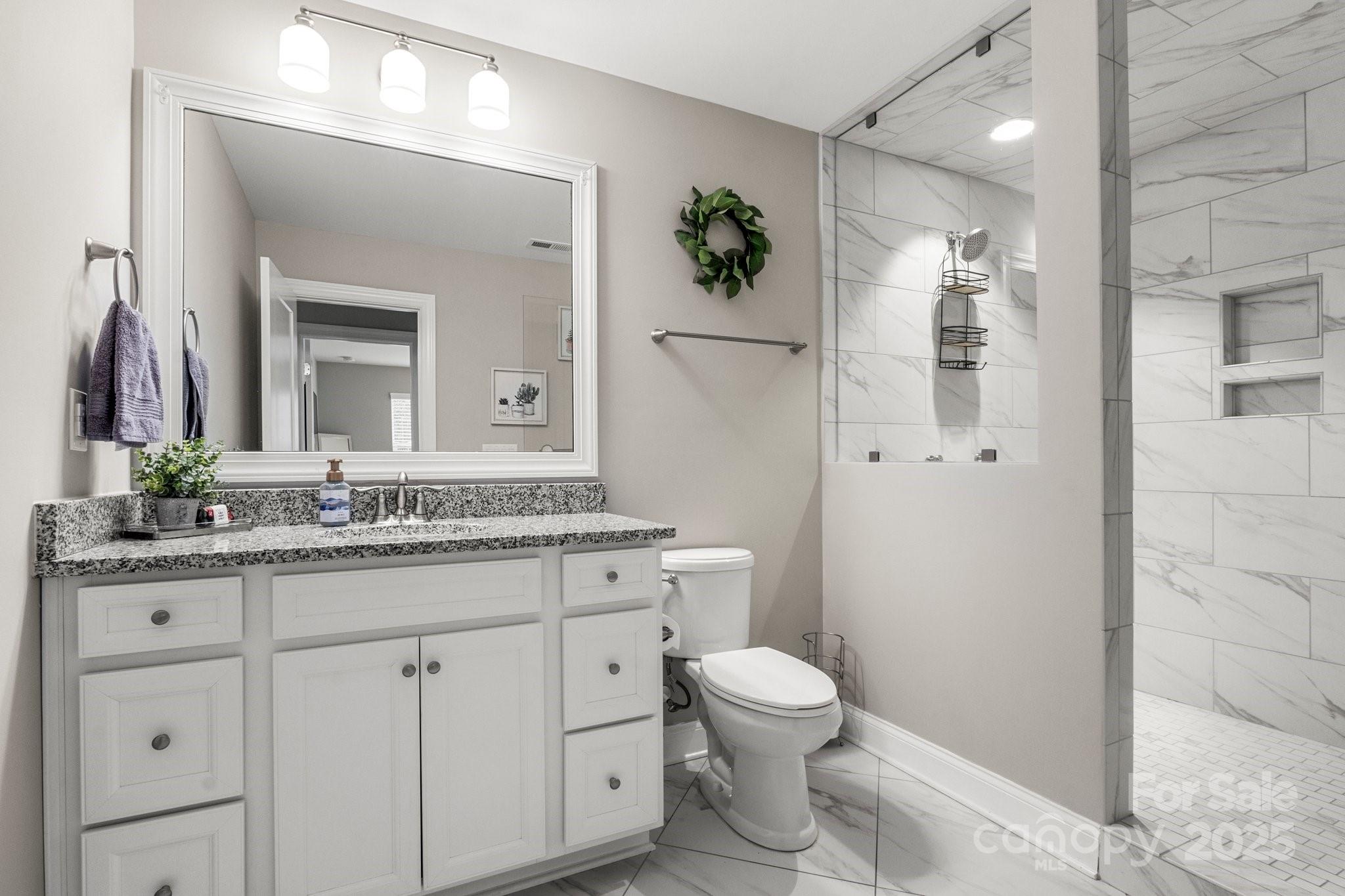 Bathroom with a granite-topped vanity and marble-look tiled walk-in shower.