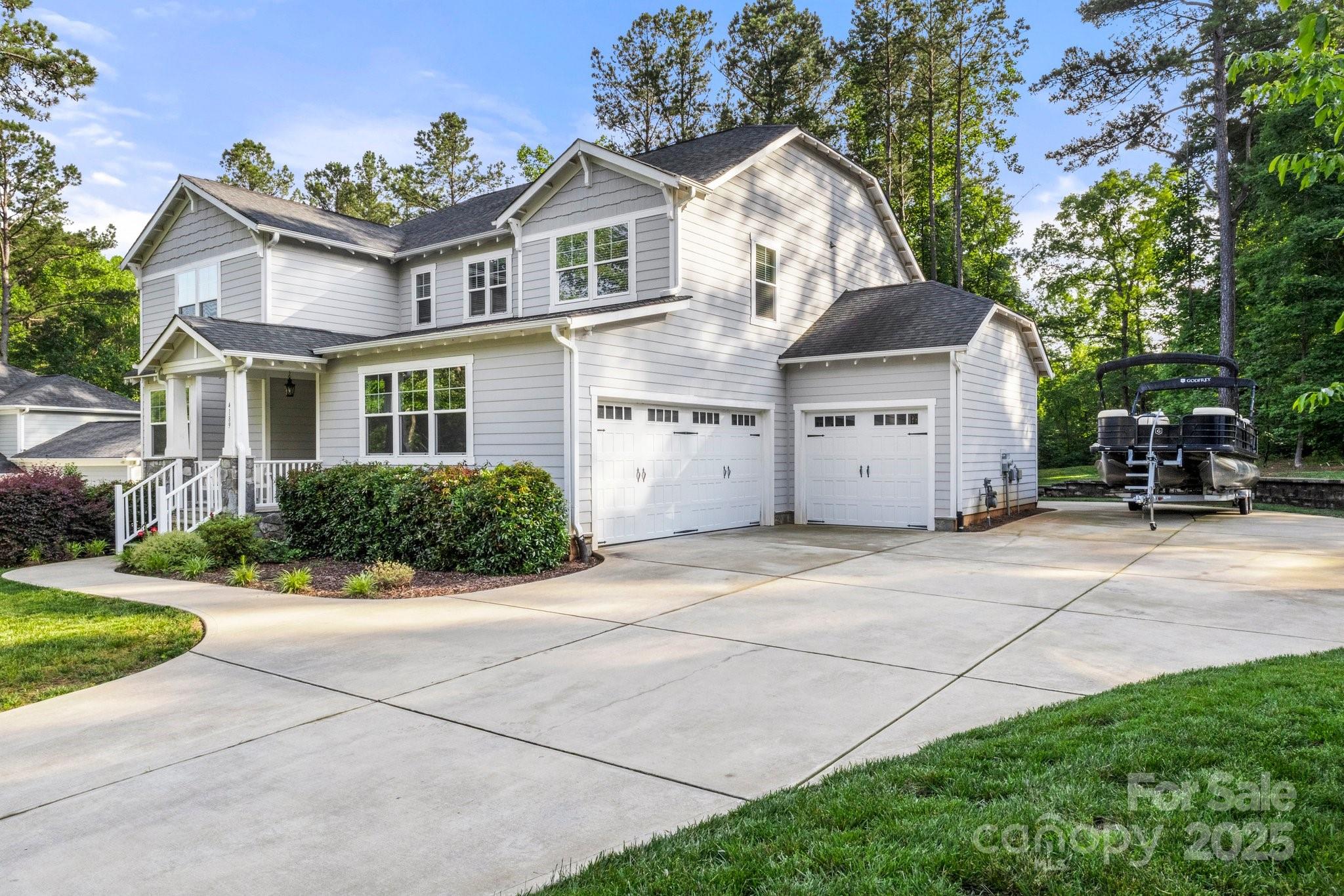 Two-story gray house with a covered porch, double garage, broad driveway, and pontoon boat on a trailer.